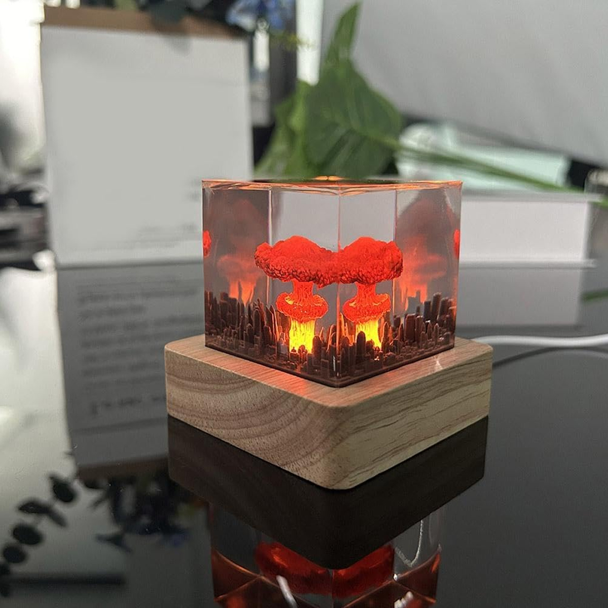 Harzwürfel auf Holzbasis mit beleuchteter Atompilz-Miniatur über einer Stadt.