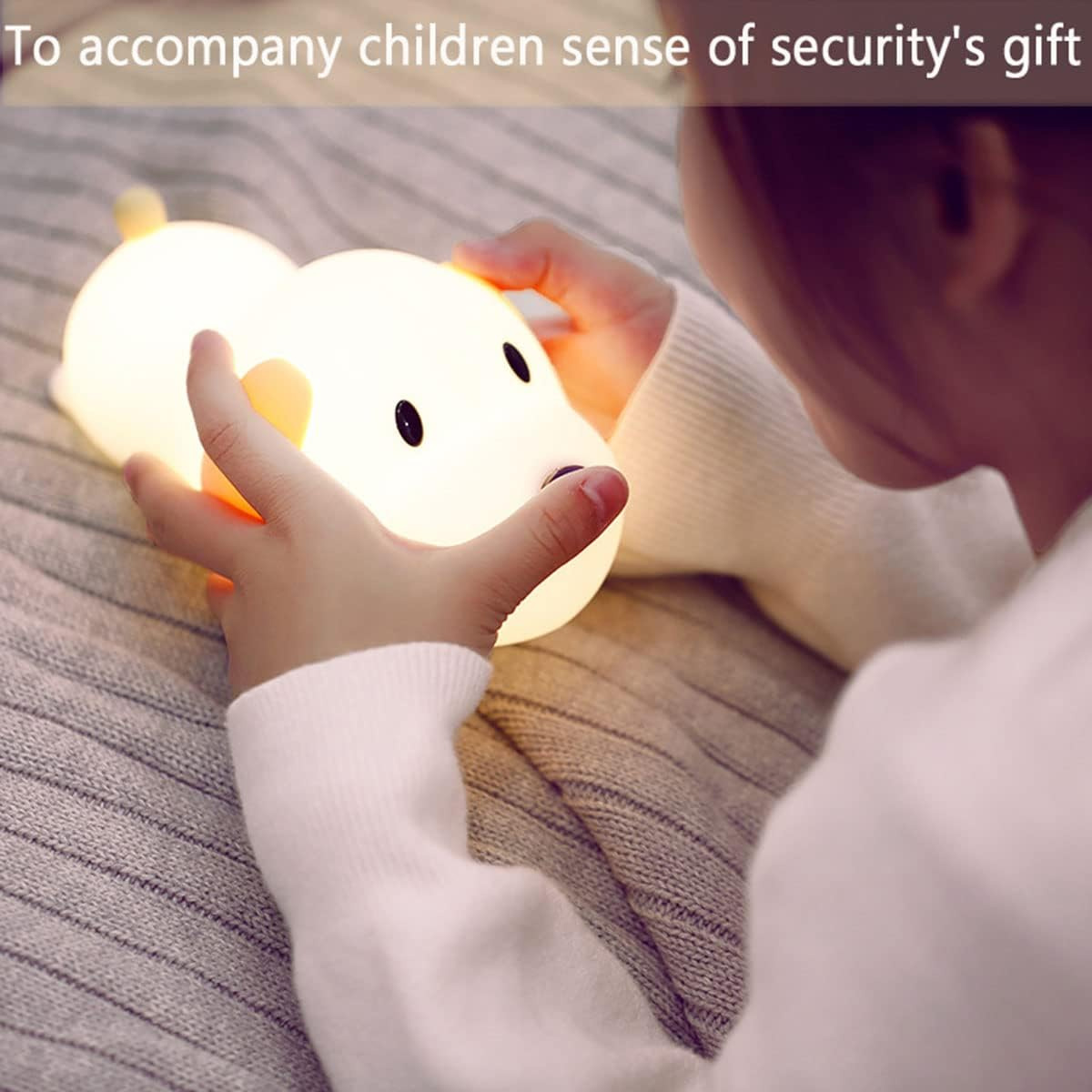 Ein Kind hält und betrachtet eine leuchtende, hundeförmige Nachtlampe auf einem Bett.
