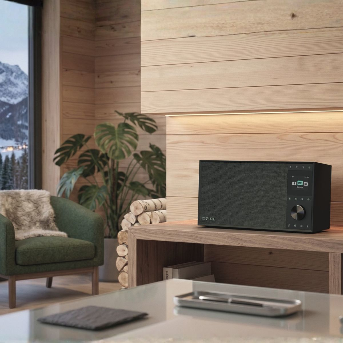 Ein schwarzes Radio auf einem Holzschrank in einem gemütlichen Raum mit grünem Sessel und verschneitem Fensterblick.