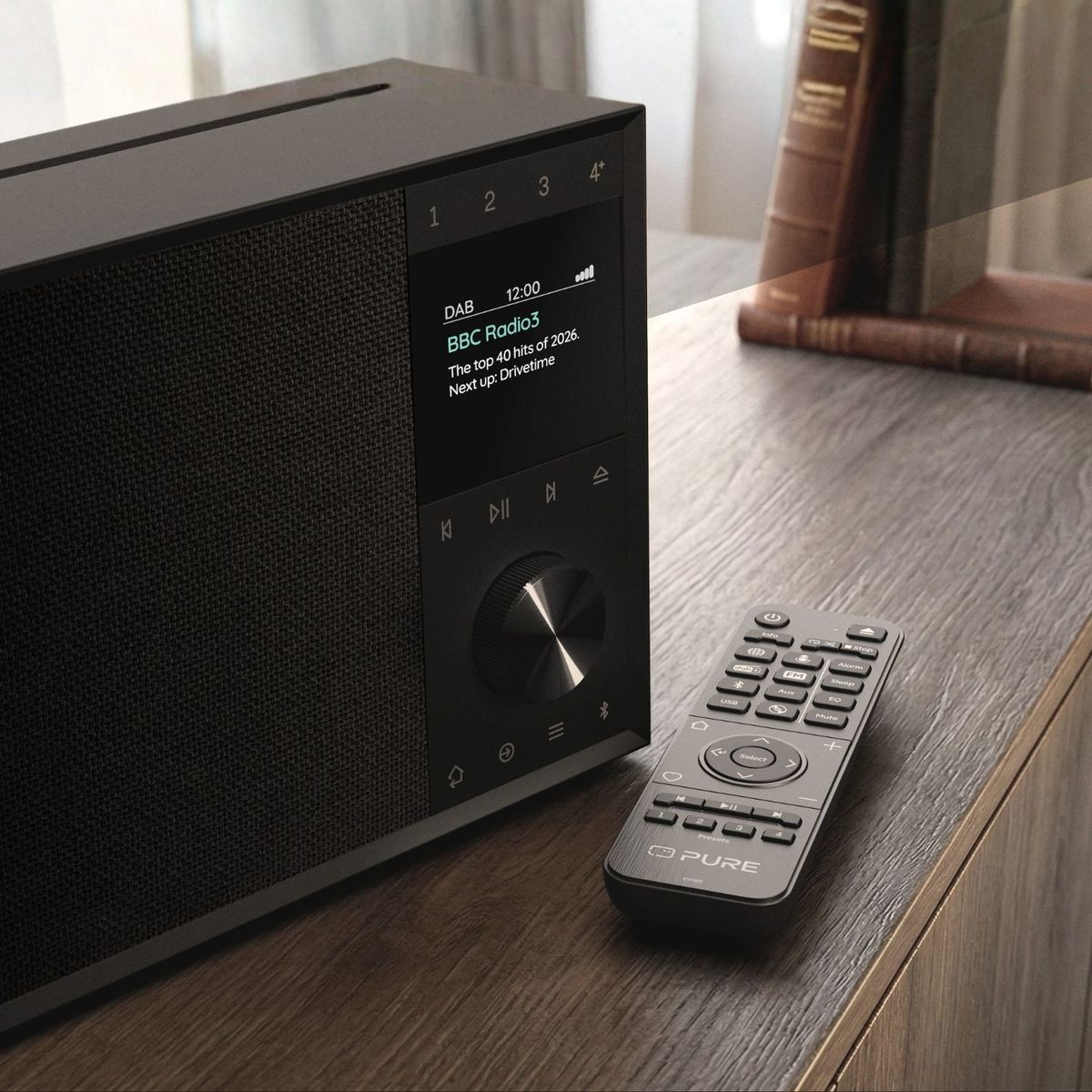 Schwarzes Digitalradio mit LCD-Bildschirm und Fernbedienung auf einem Holzmöbelstück.