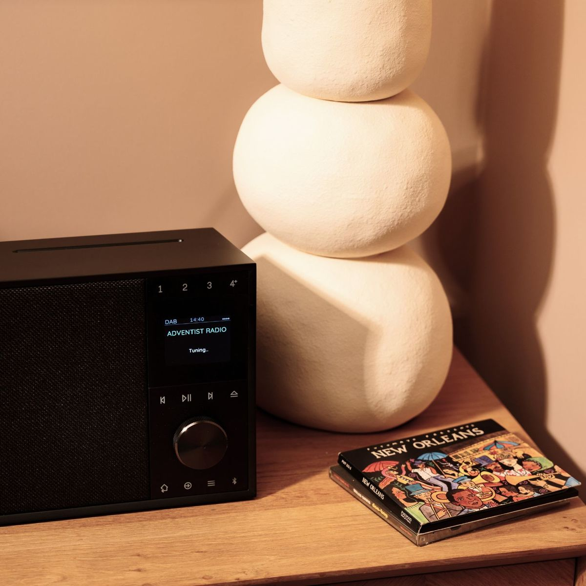 Ein schwarzes Radio, eine weiße, skulpturale Lampe und eine CD-Hülle liegen auf einer Holztischplatte.