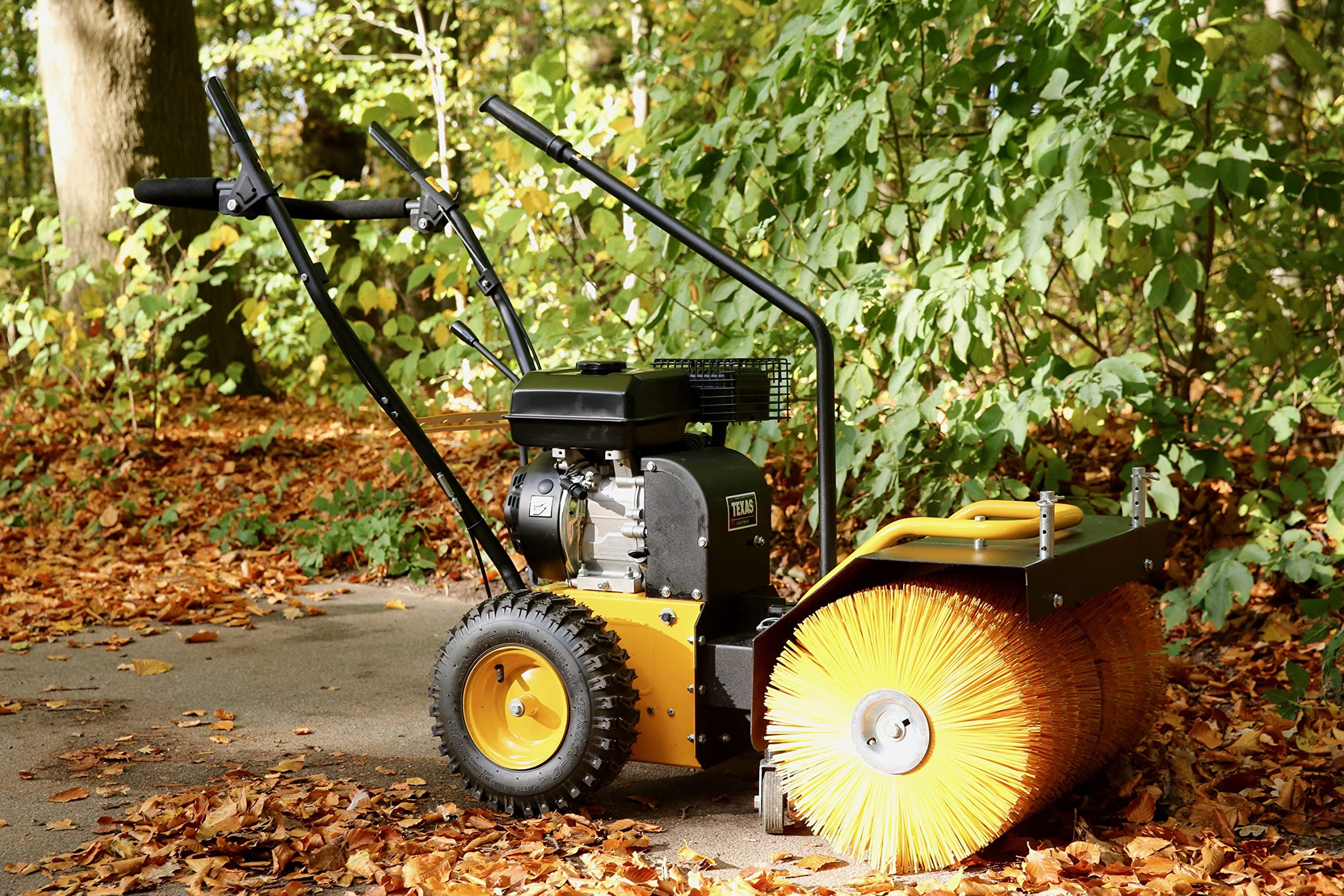 Eine gelbe Motorbürste steht im Herbstwald auf einem Weg mit Laub.