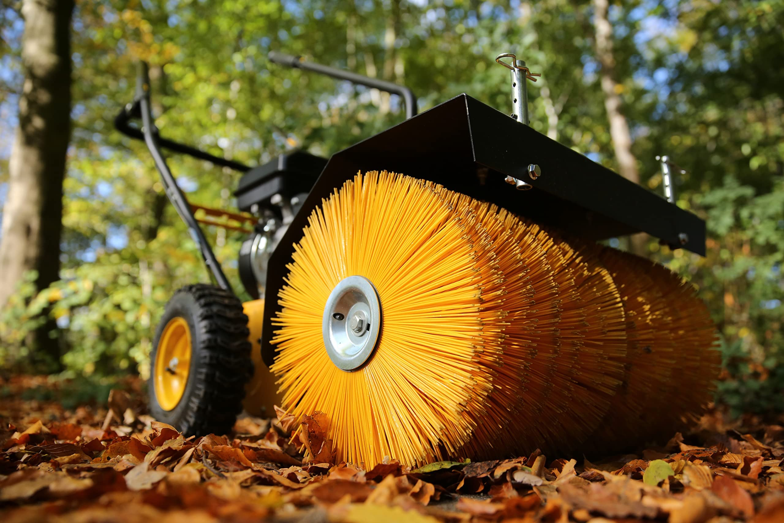 Eine gelbe Motorbürste steht im Herbstwald auf trockenem Laub.