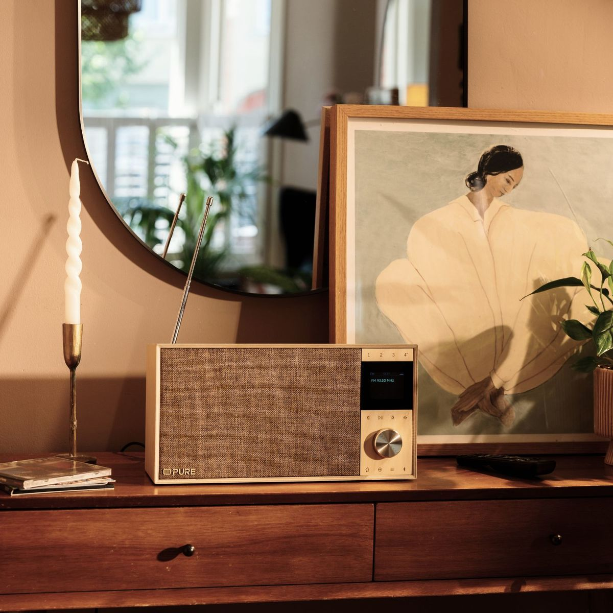 Ein Holzradio steht auf einem Sideboard neben einem gerahmten Porträt, einer Kerze und einem Spiegel.