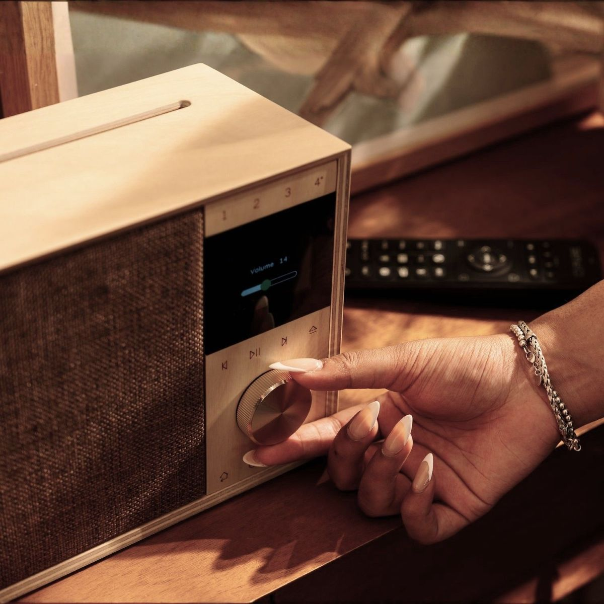 Eine Hand dreht den Lautstärkeregler an einem modernen Holzradio auf einem Tisch.