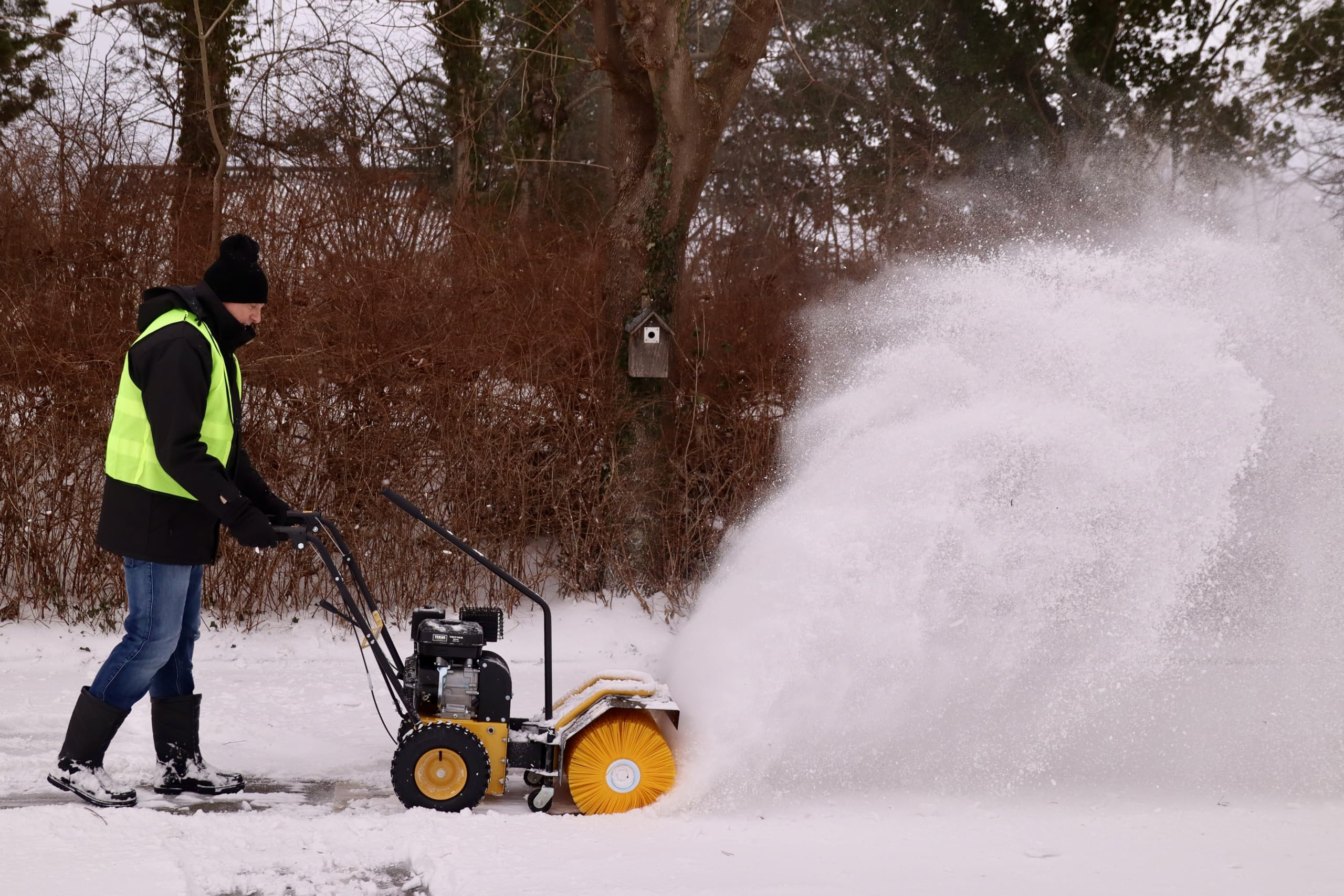Ein Mann im Winterkleidung bedient eine motorisierte Schneefräse, die Schnee aufwirbelt.