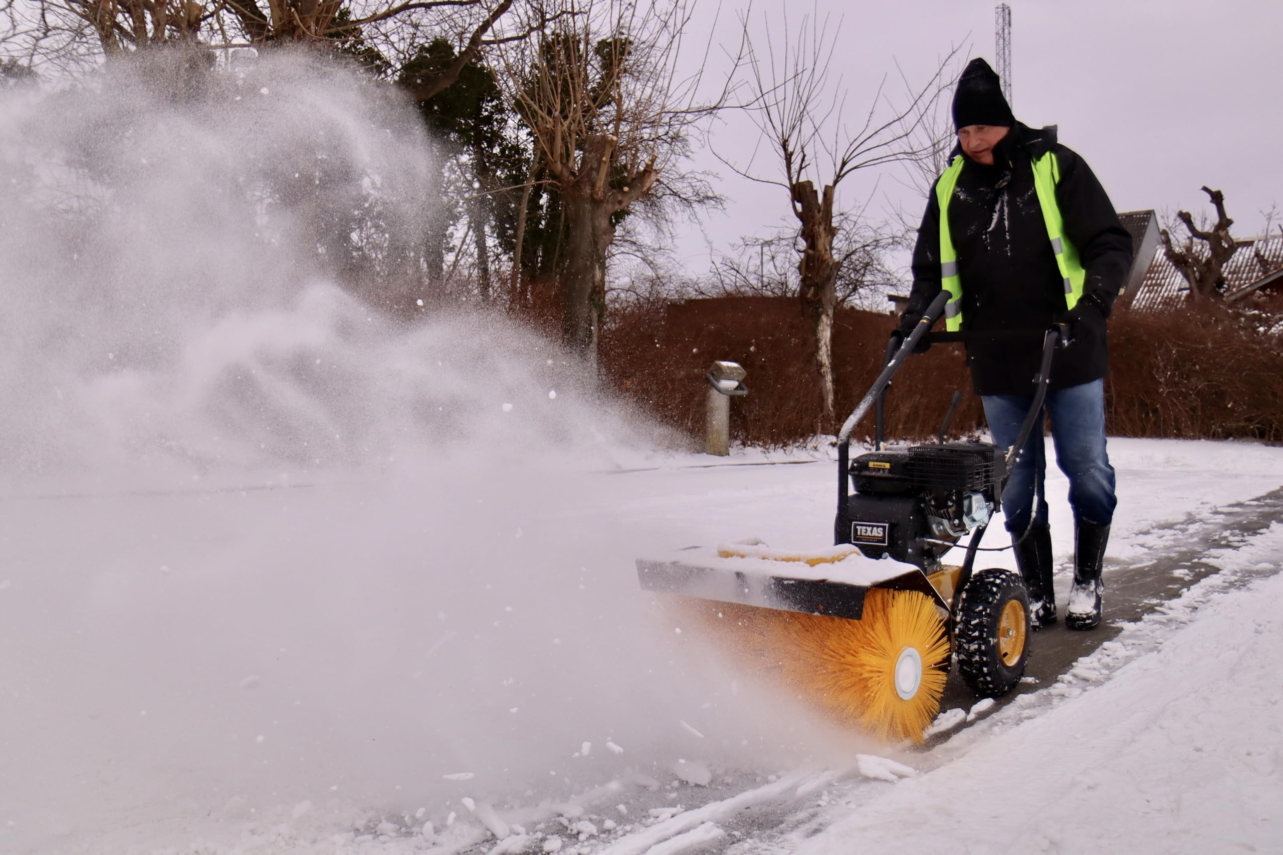 Ein Mann in schwarzer Jacke und gelber Weste bedient eine motorisierte Kehrmaschine im Schnee.