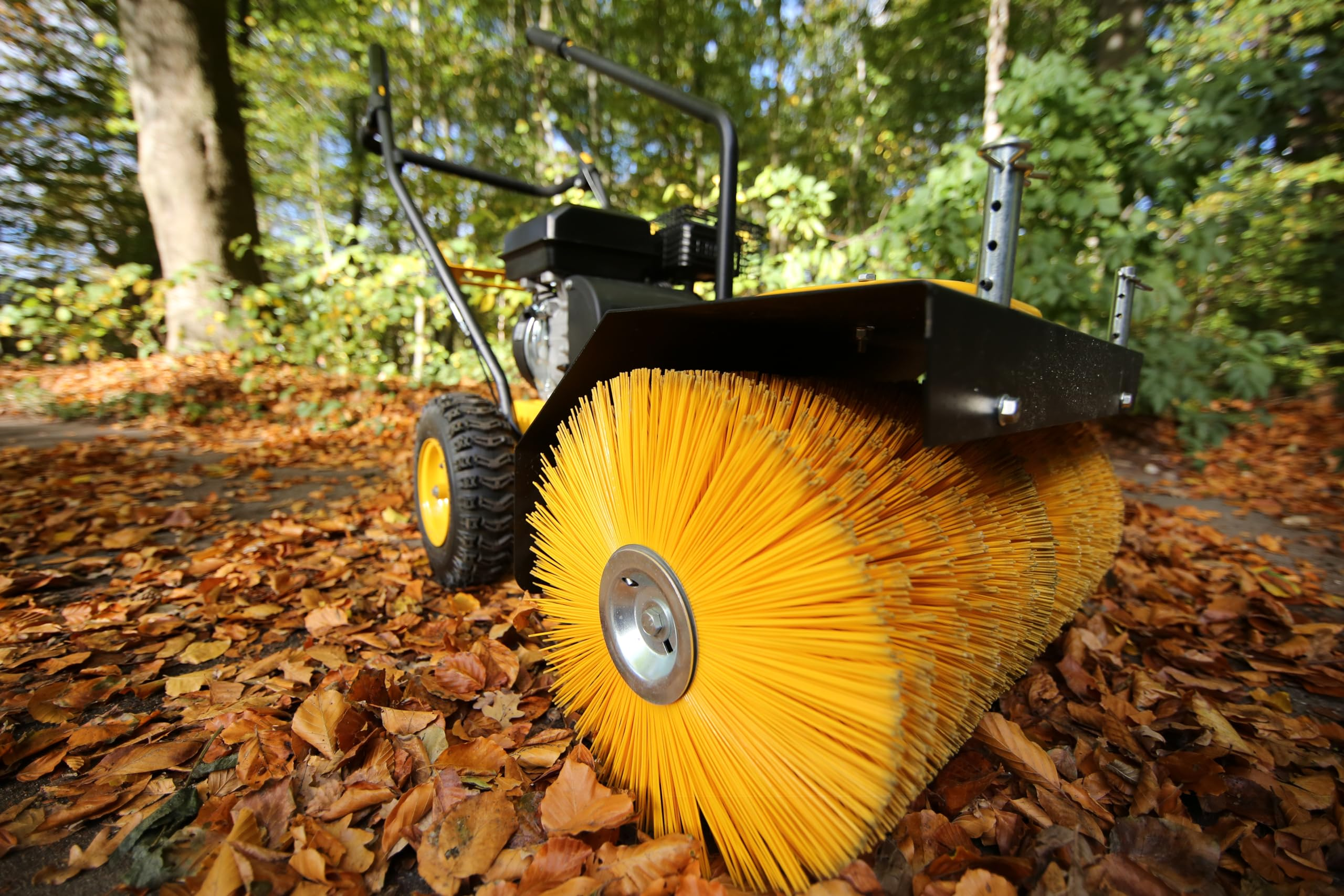 Eine gelbe Motorbürste steht im Herbst auf mit Laub bedecktem Boden.