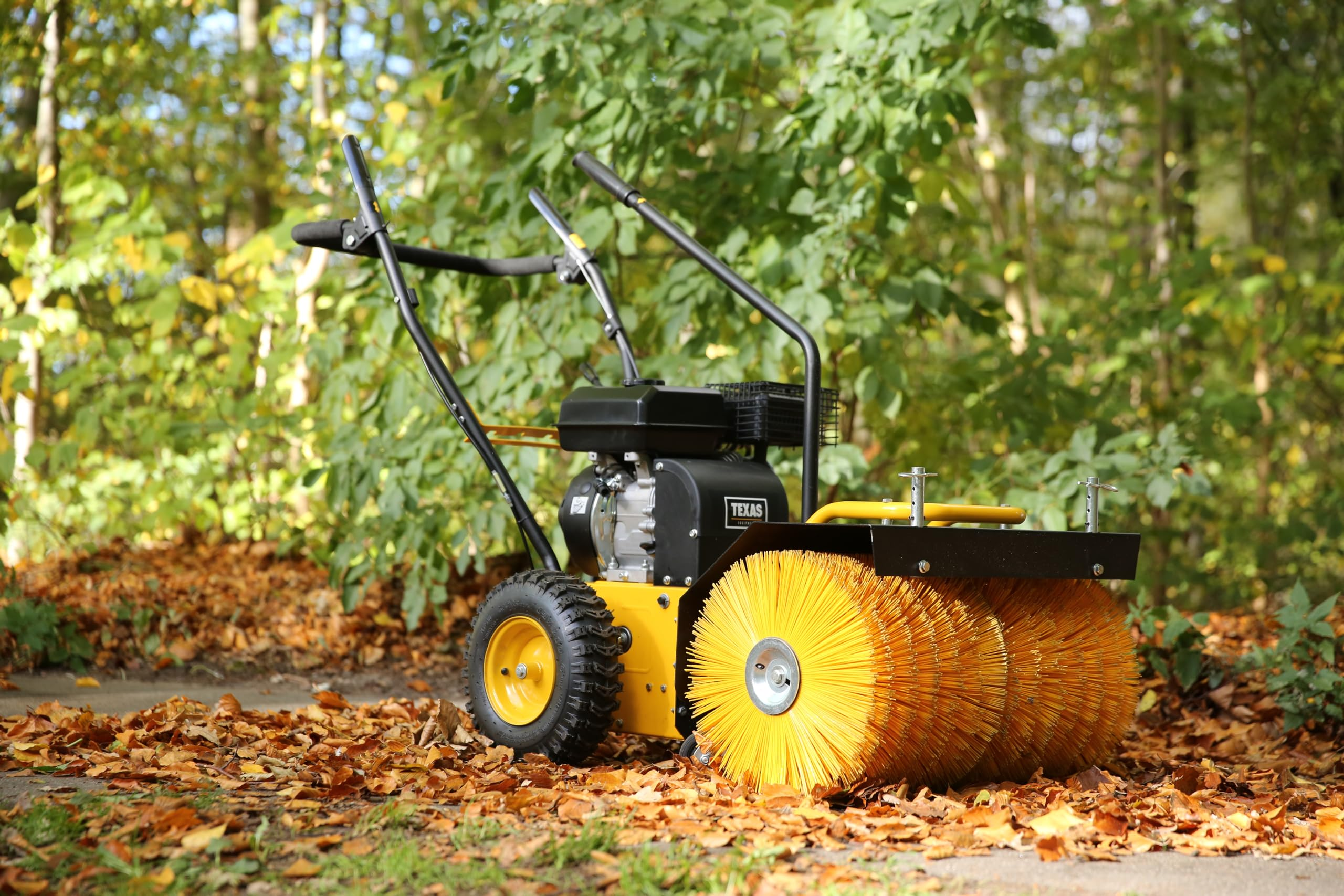 Gelbe Motorbürste auf von Laub bedecktem Weg vor grünem Wald.