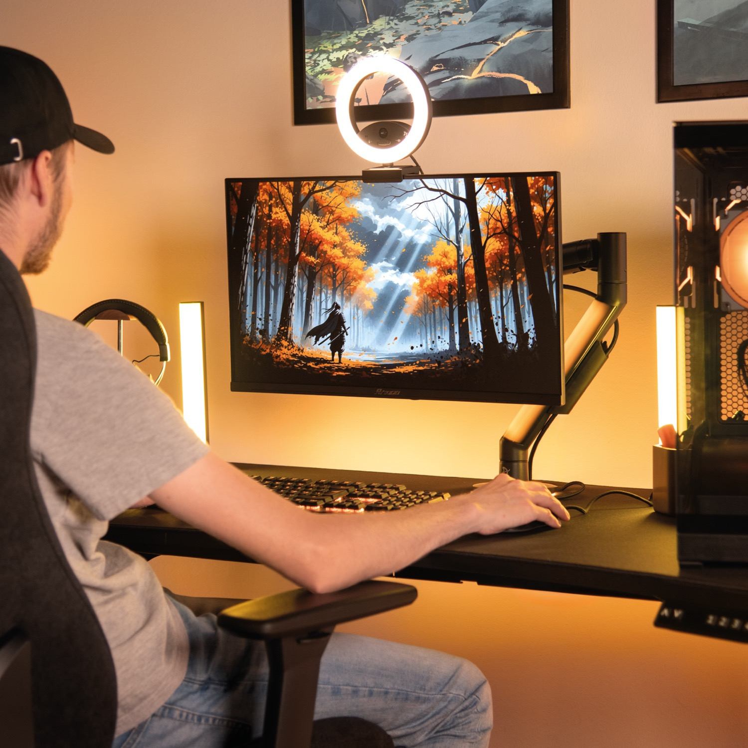 Un uomo gioca a una scrivania con due monitor, luce anulare e calda illuminazione.