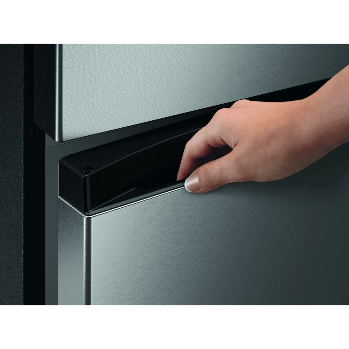 Una mano abre el cajón de un refrigerador de acero inoxidable moderno.