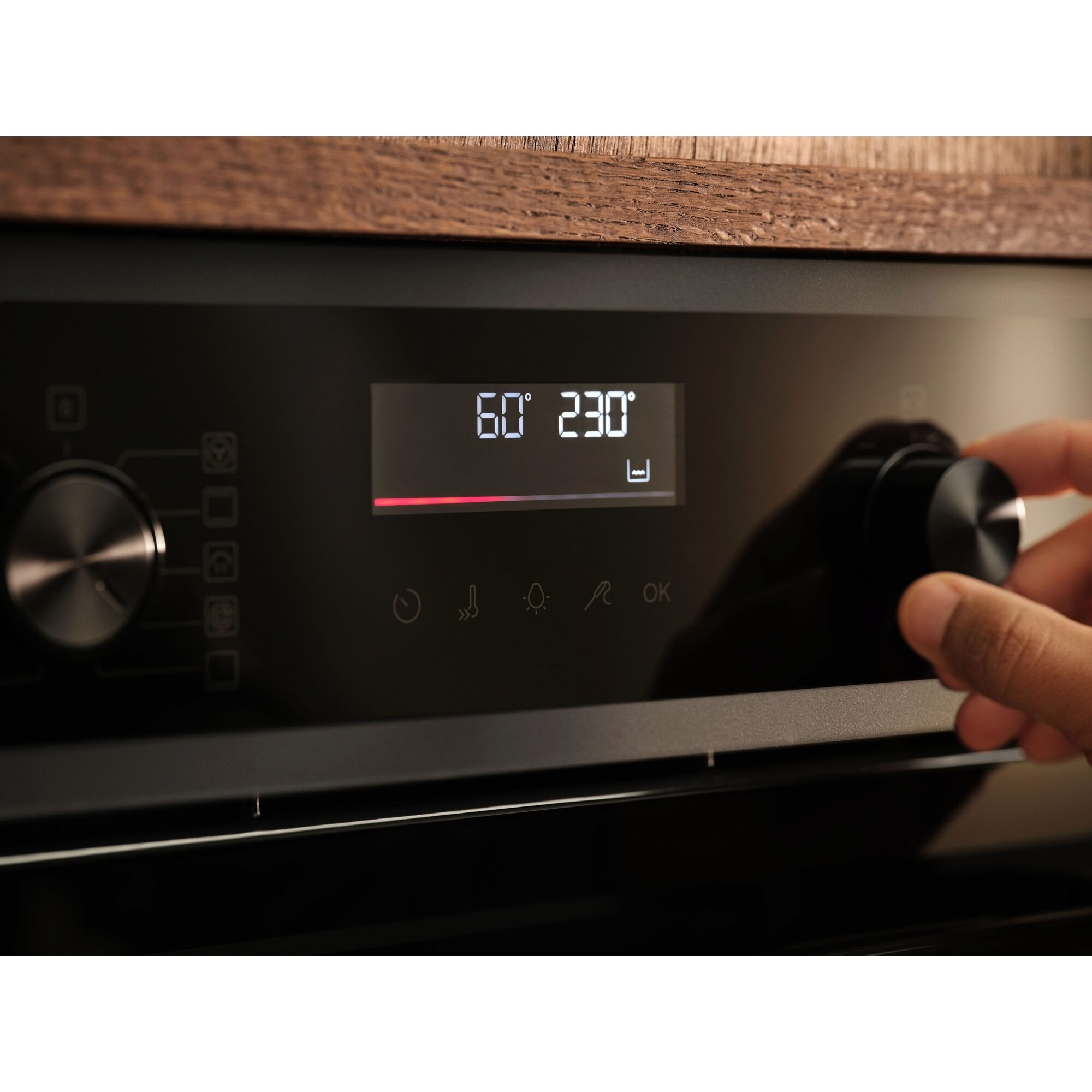Mano girando un mando negro en un horno moderno con pantalla digital.