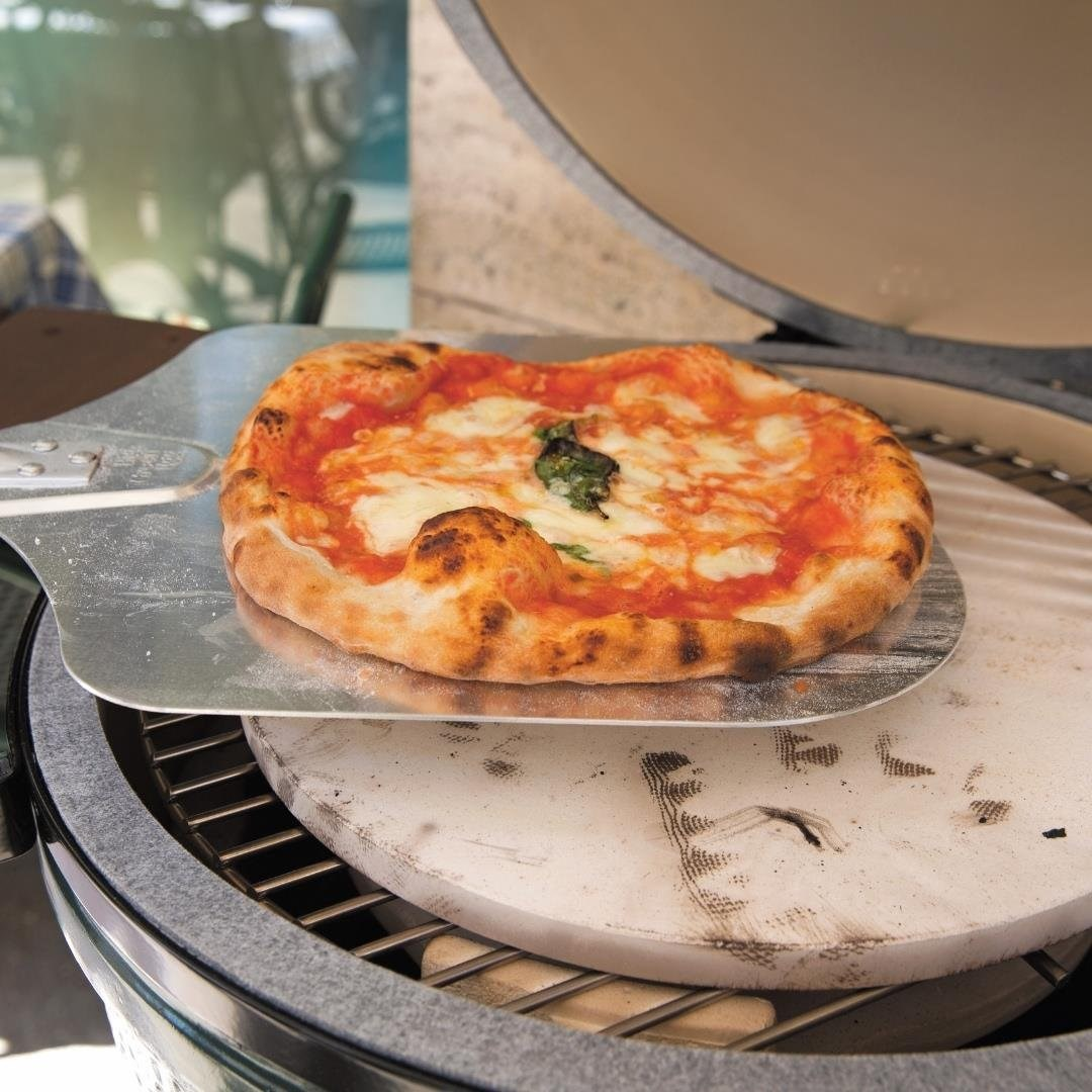 Açık bir pizza fırınına metal kürekle yerleştirilen taze bir pizza.
