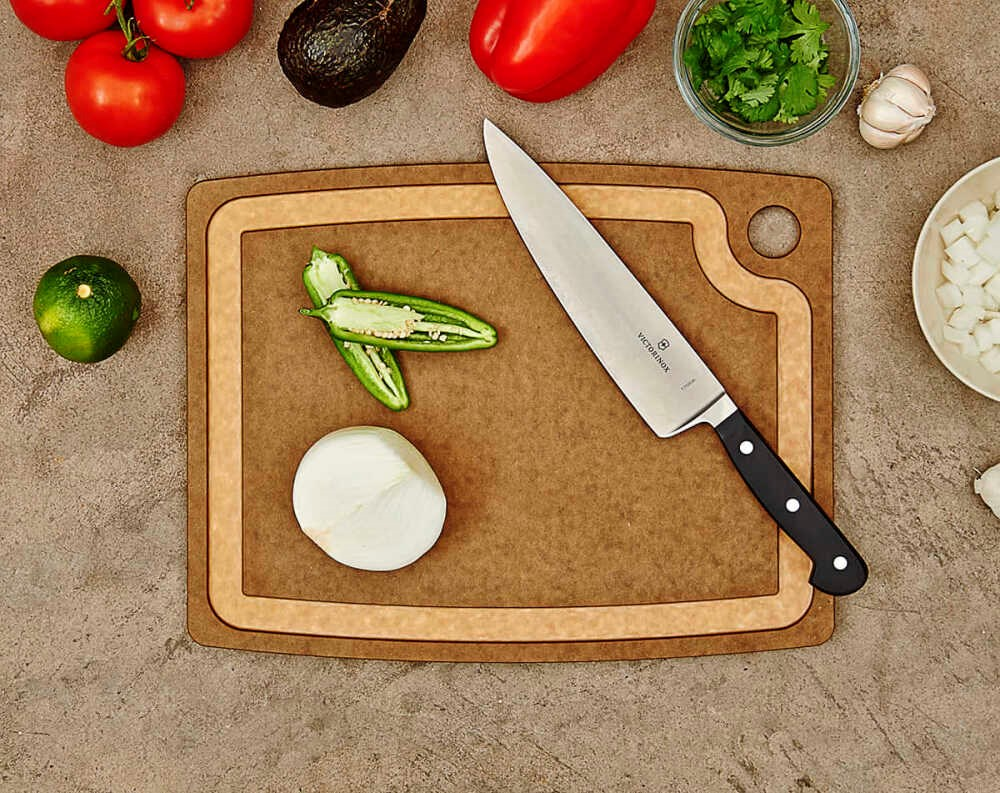 Kesme tahtası üzerinde bir şef bıçağı, yarım soğan ve jalapeno, tezgahta sebzelerle çevrili.