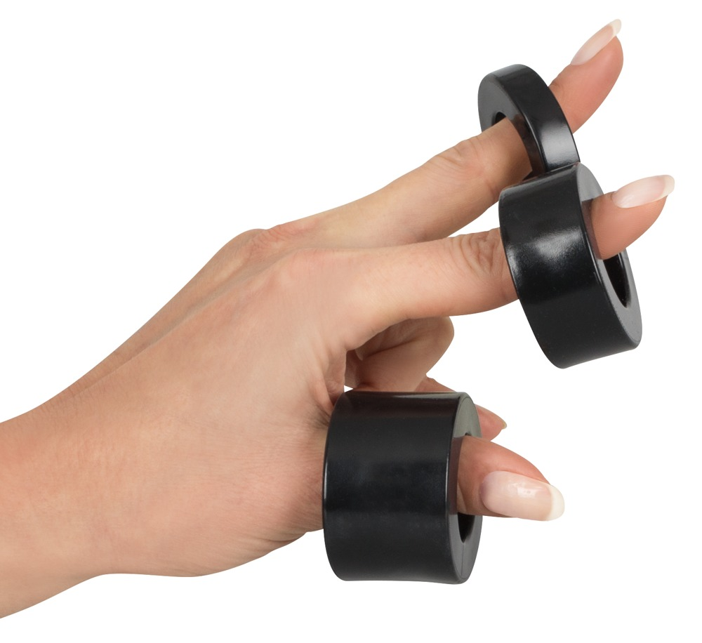 Eine Hand trägt schwarze Gewichtsringe an zwei Fingern auf weißem Hintergrund.