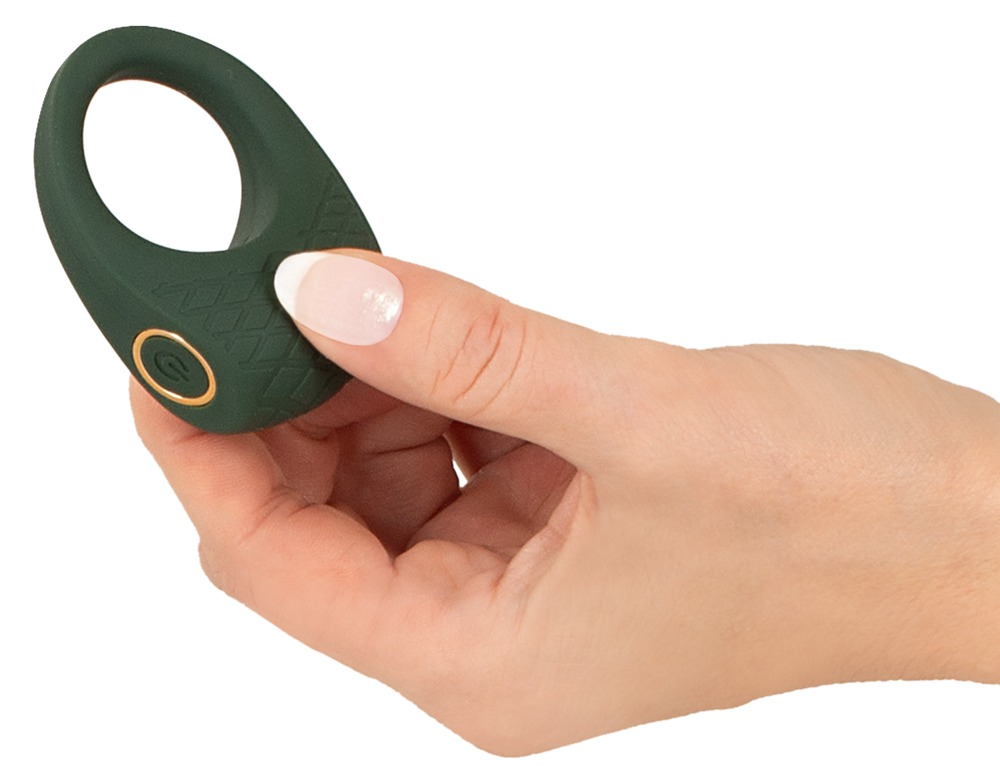 Eine Hand hält ein kleines, dunkelgrünes Sexspielzeug in Ringform mit einem goldenen Einschaltknopf auf weißem Hintergrund.