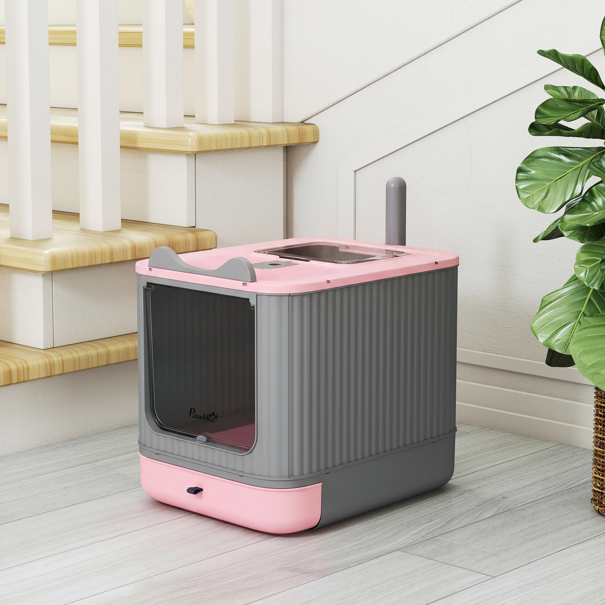 Un arenero para gatos cerrado de color rosa y gris sobre suelo de madera clara junto a unas escaleras y una planta.