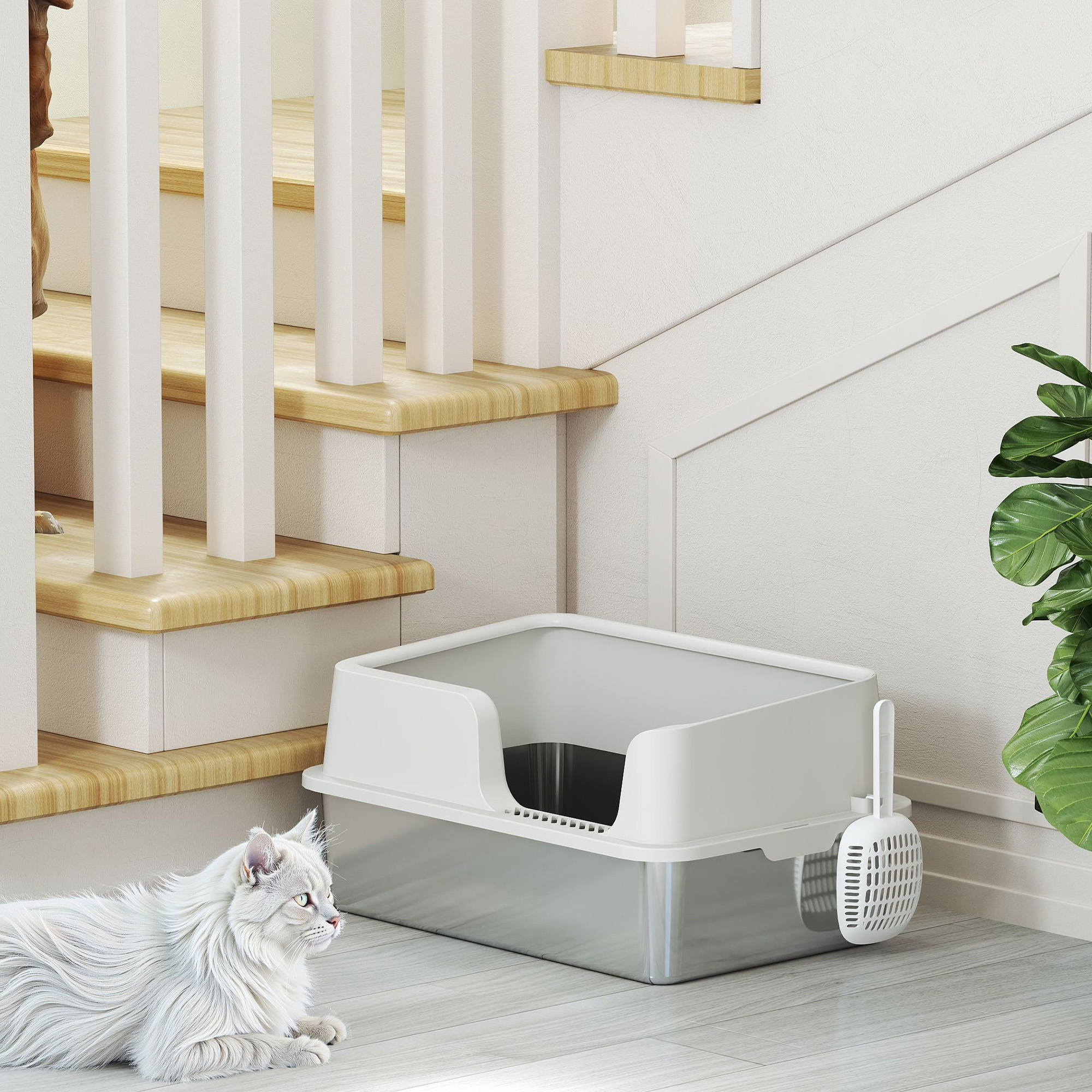Un gato blanco yace frente a un arenero con pala, colocado junto a unas escaleras de madera clara y una planta.