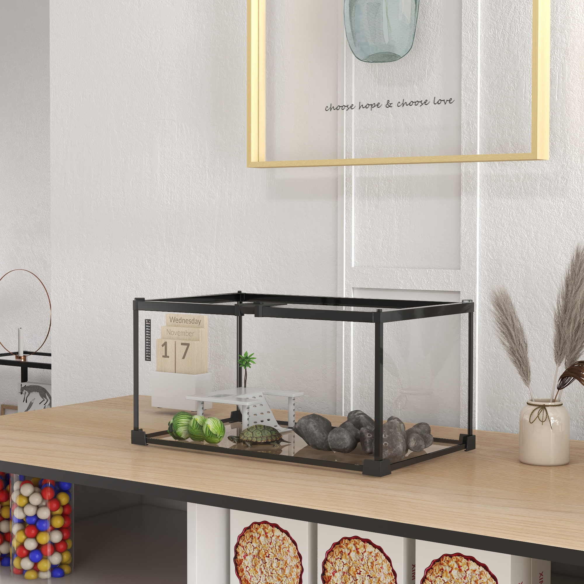 Un pequeño terrario para tortugas en un escritorio de madera con rocas, una mini palmera y un calendario al fondo.