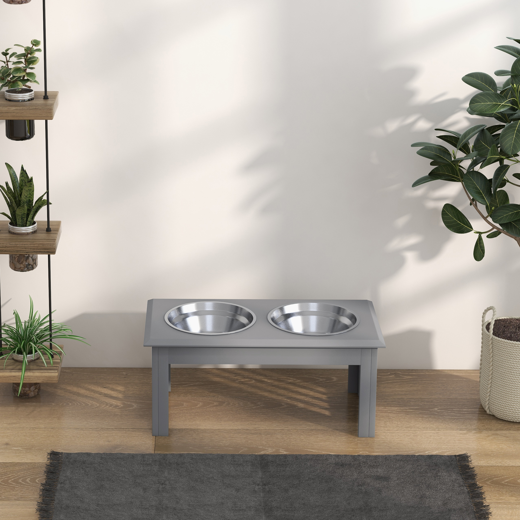 Comedero elevado gris para mascotas con dos cuencos de metal, flanqueado por plantas y una alfombra.