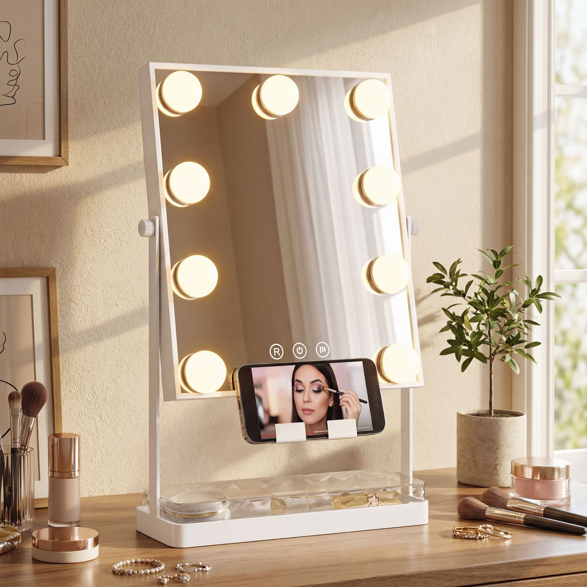 Un espejo de maquillaje con luces sobre un escritorio de madera con soporte para teléfono, brochas y una planta.