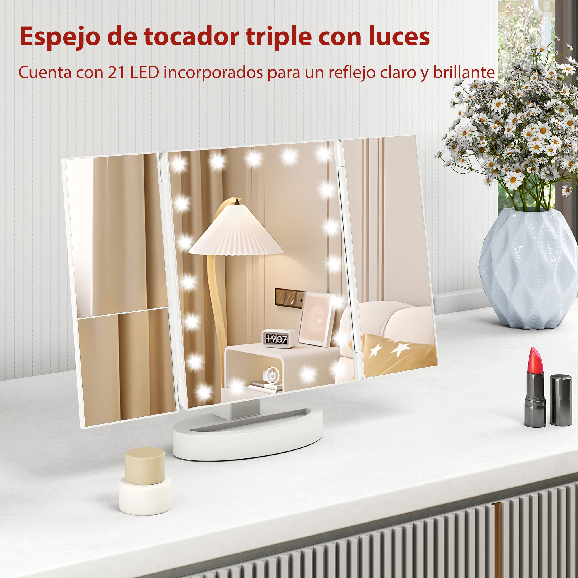 Un espejo de tocador triple con luces está sobre una mesa blanca, junto a un jarrón y lápiz labial.