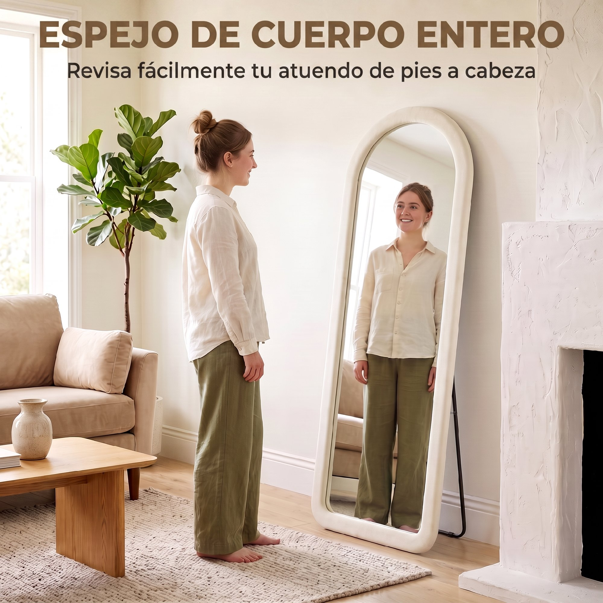 Una mujer con blusa blanca y pantalones verdes se para frente a un espejo de cuerpo entero ovalado en una sala luminosa.