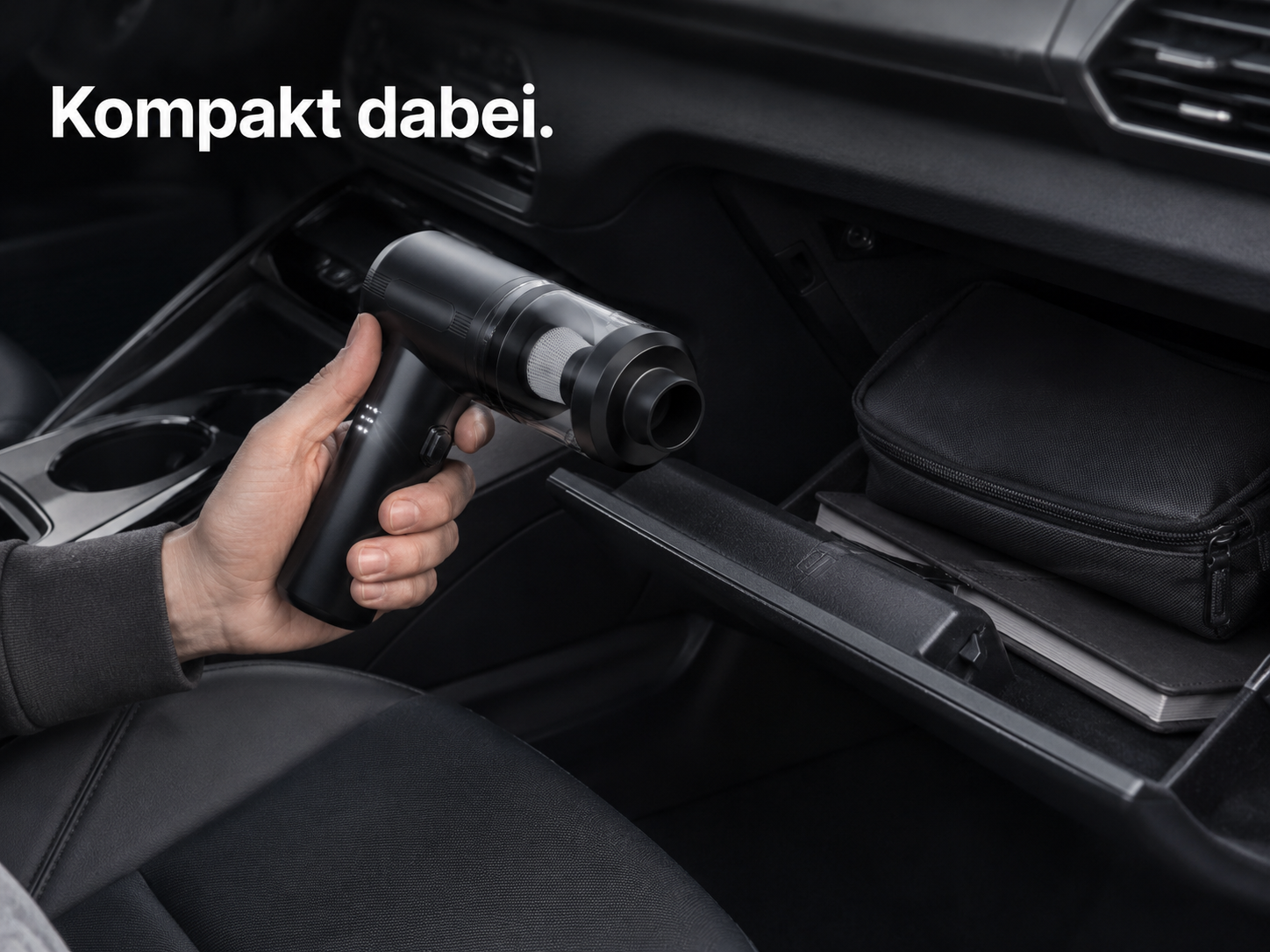 Eine Hand hält einen kompakten schwarzen Handstaubsauger in einem Auto. Text: 'Kompakt dabei'.