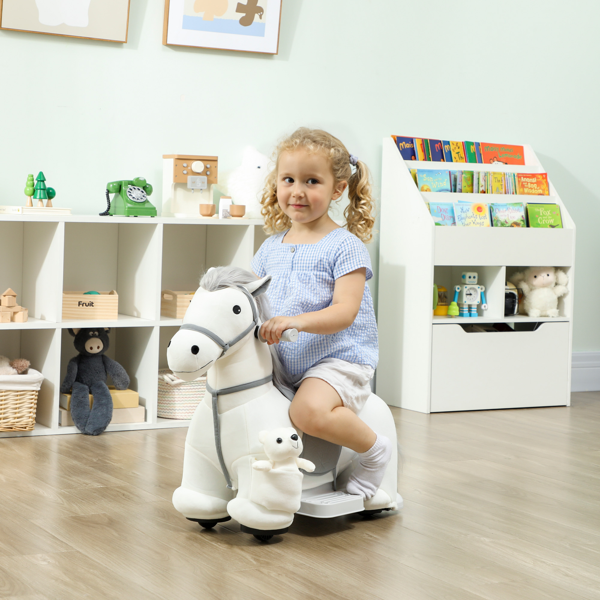 Una niña rubia montando un caballo de peluche en una habitación infantil llena de juguetes.
