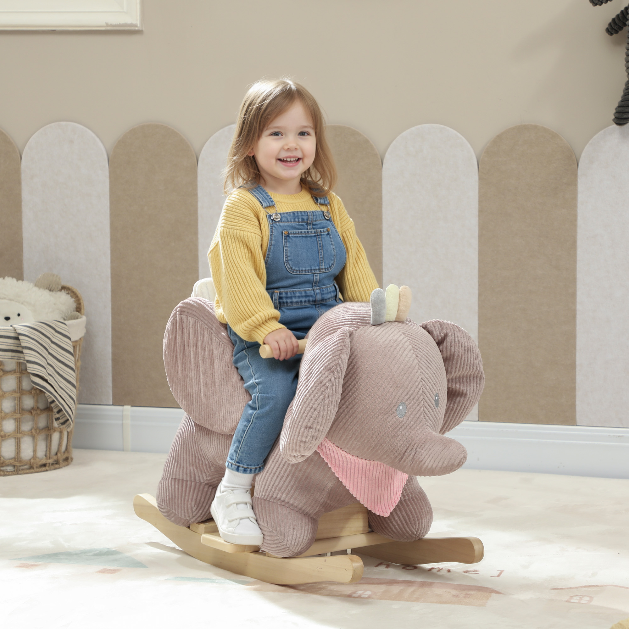 Niña sonriendo sentada en un balancín de peluche con forma de elefante en una habitación infantil.