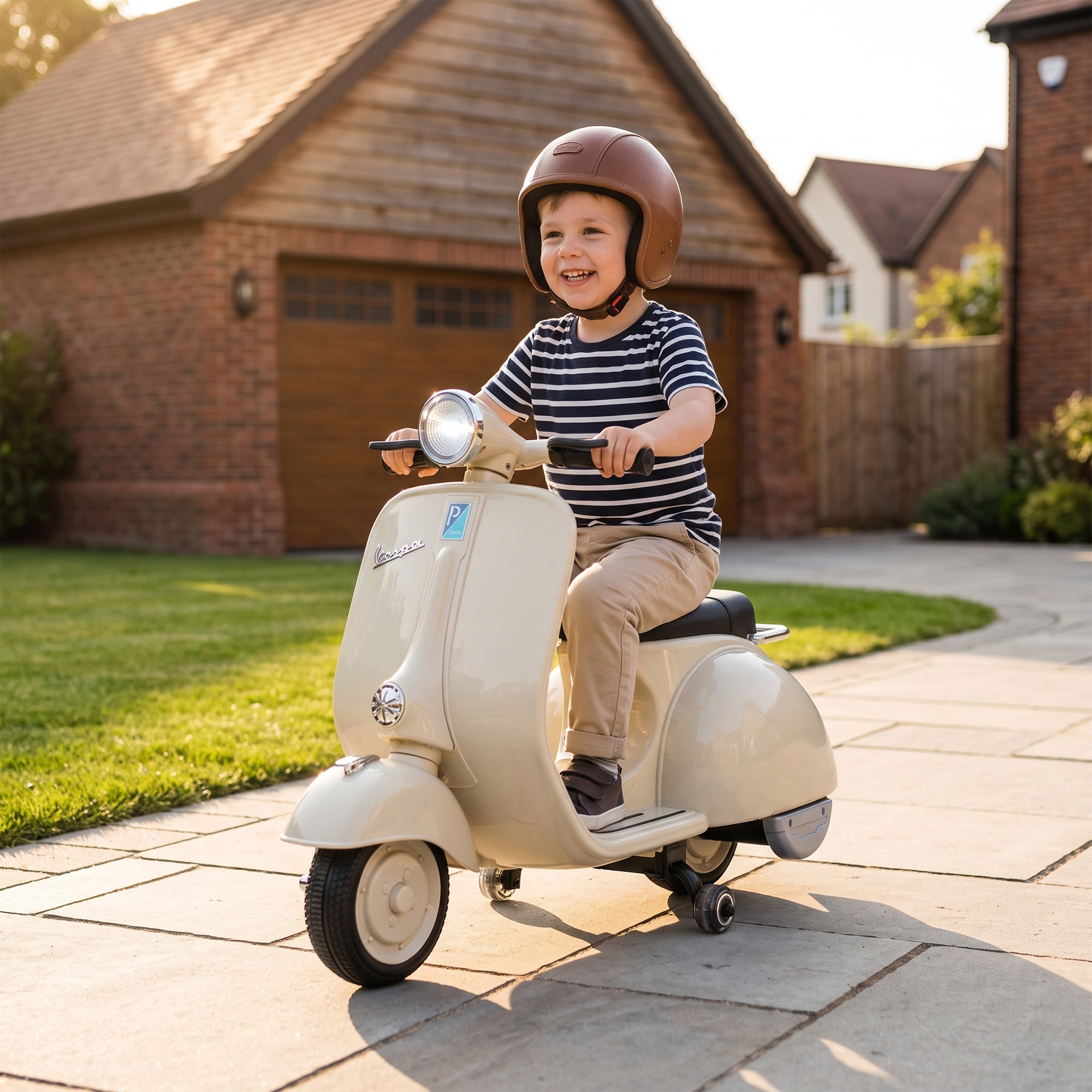 Un niño sonriente con casco marrón monta en un pequeño patinete Vespa crema en una entrada frente a una casa.