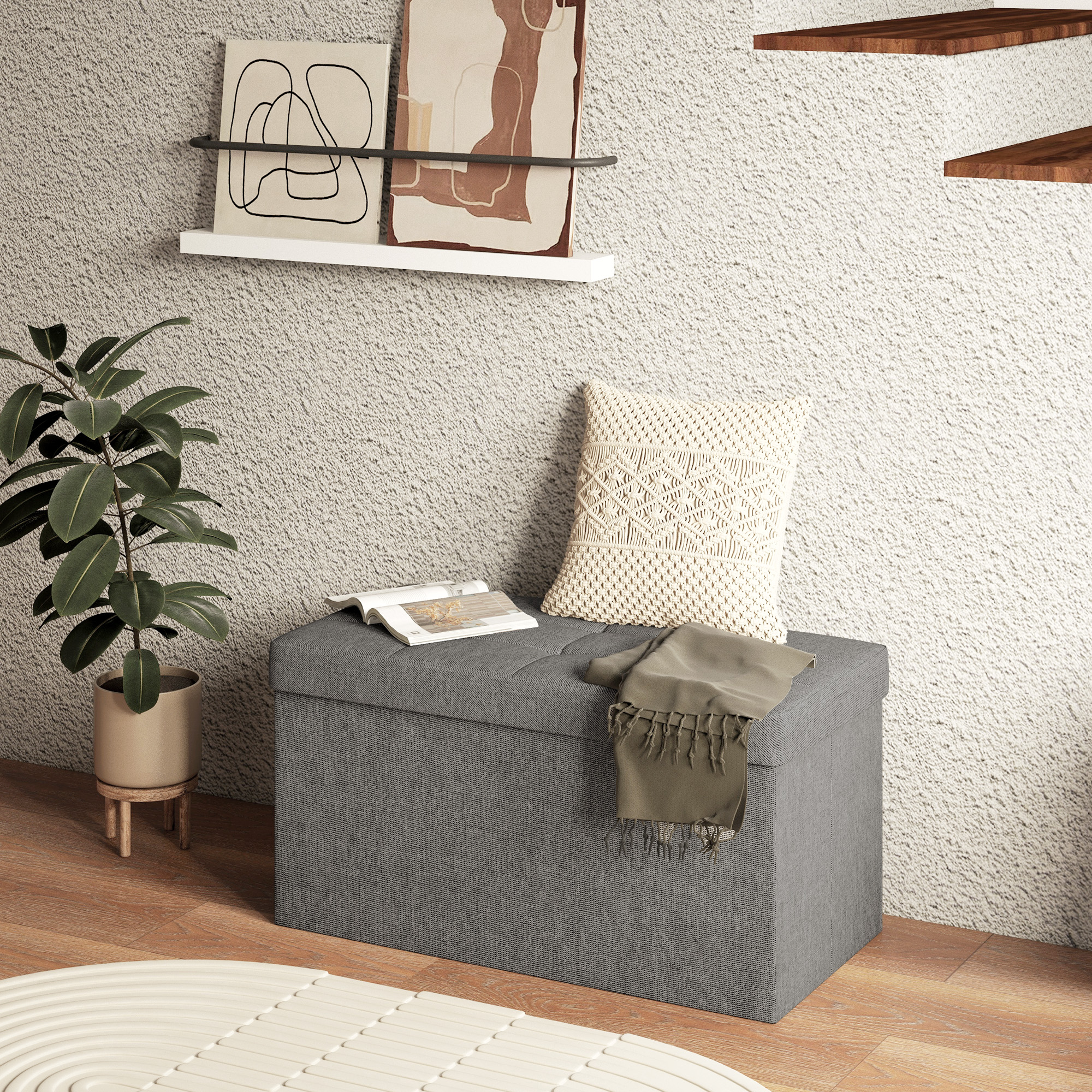 Un banco de almacenamiento gris con cojín, libro y manta, junto a una planta en pared texturizada.