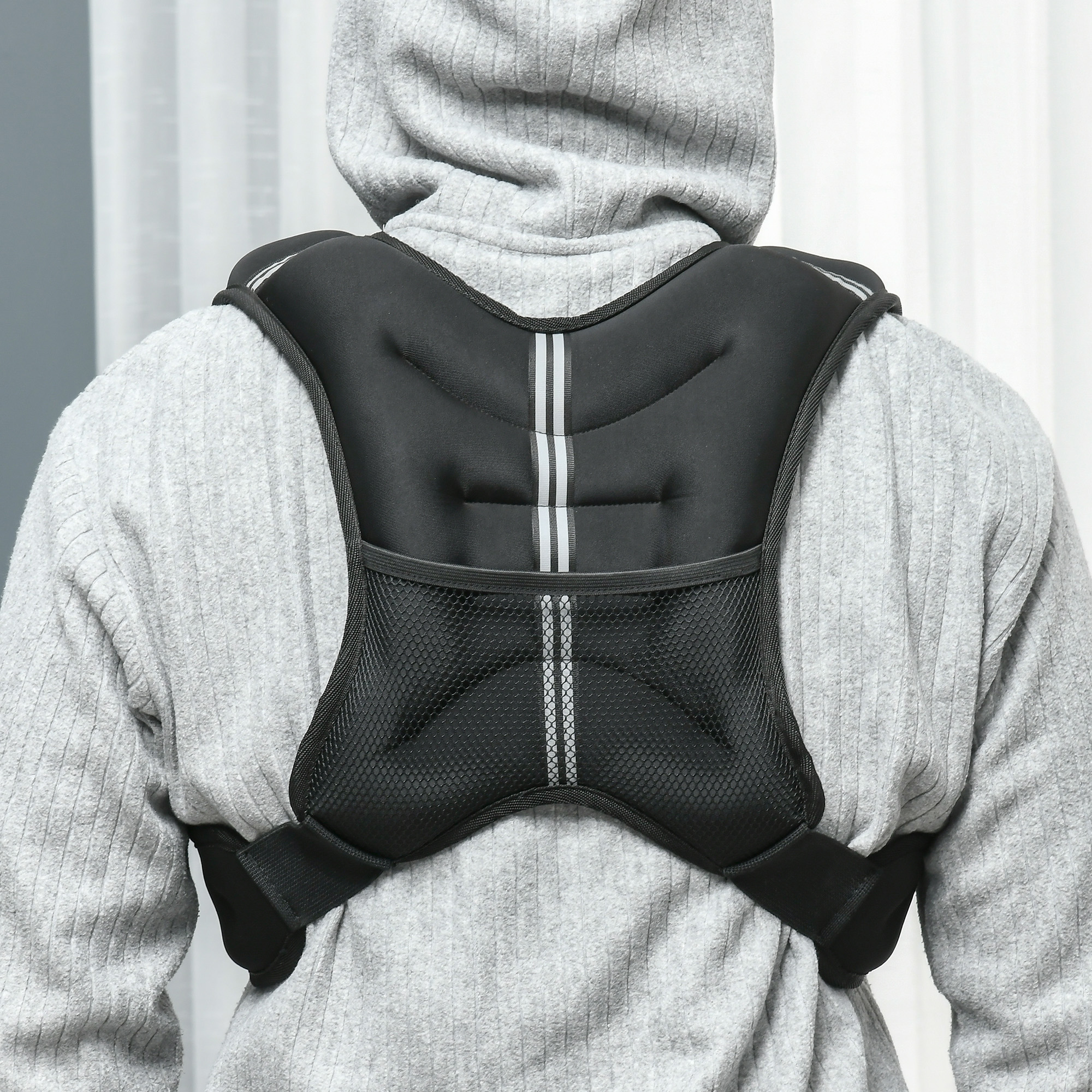 Una persona con sudadera gris lleva un chaleco con peso negro y rayas reflectantes.