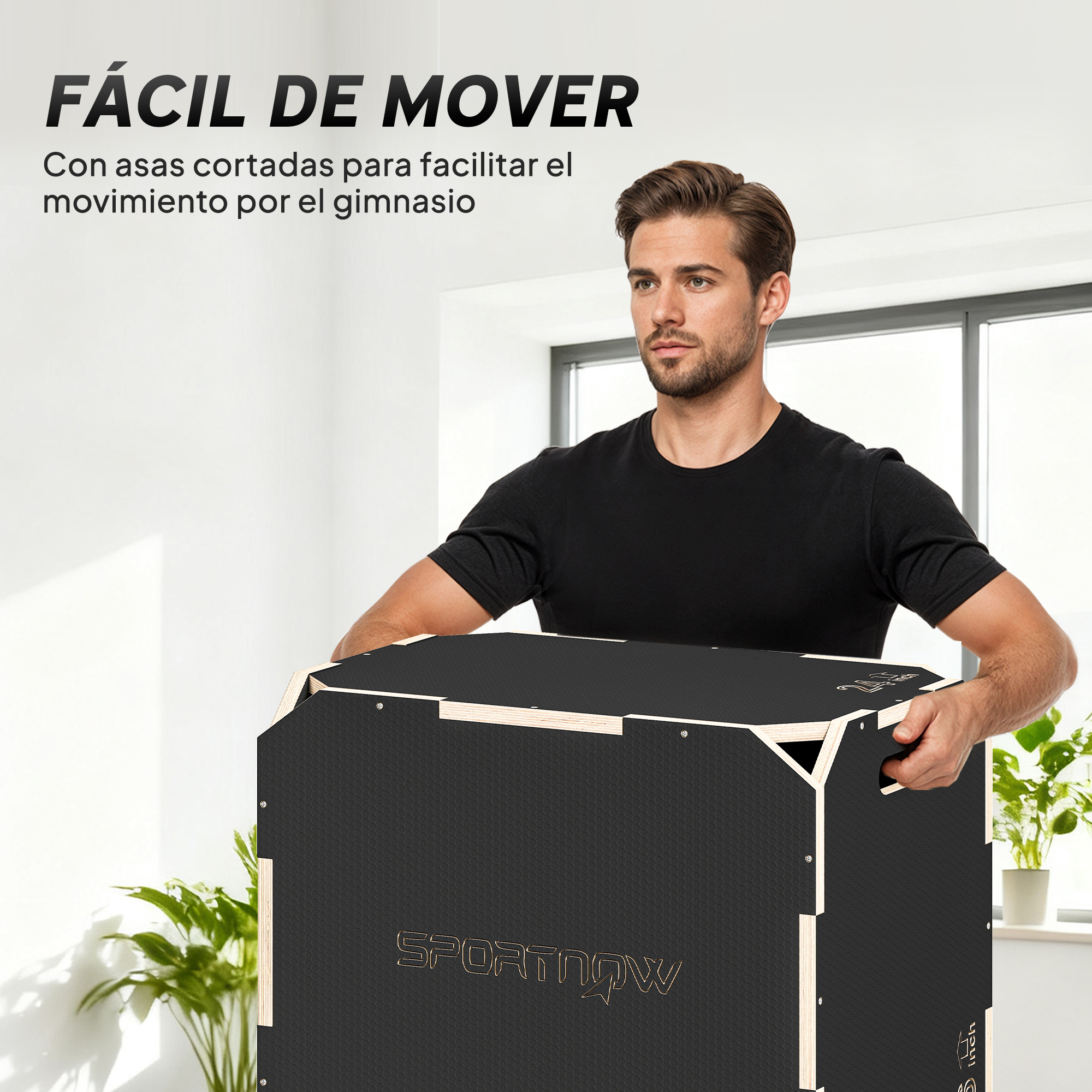 Un hombre con camiseta negra sostiene una gran caja pliométrica de madera en una habitación luminosa.