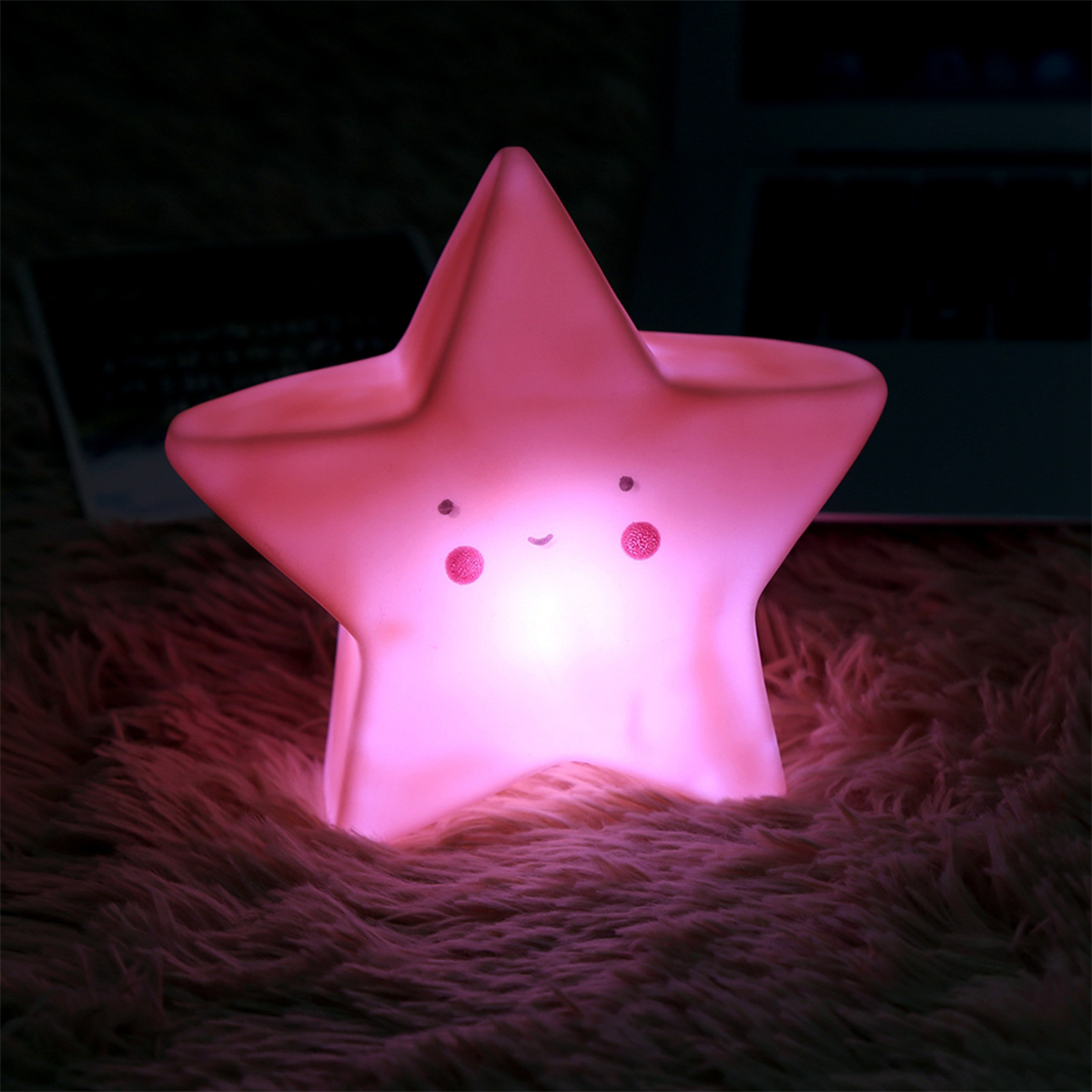 Eine rosafarbene, leuchtende Sternlampe mit niedlichem Gesicht sitzt auf einem flauschigen Teppich.