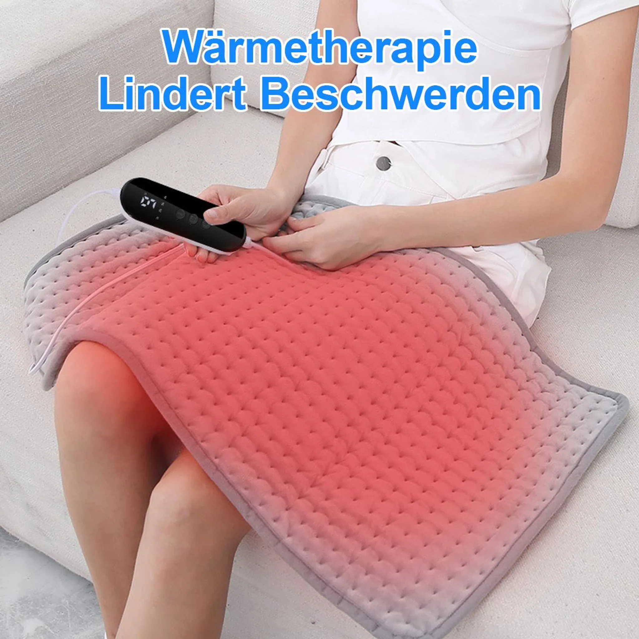 Eine Person sitzt auf einem Sofa und hält die Steuerung eines roten Heizkissens auf ihren Beinen.