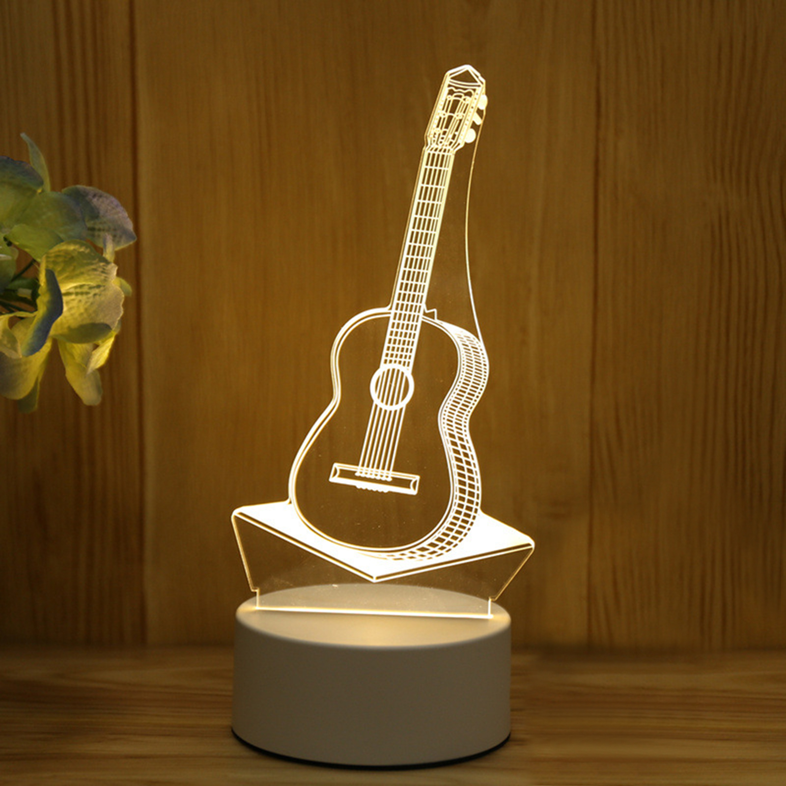 Eine leuchtende Acrylgitarrenlampe steht auf einem weißen Sockel vor einer Holztafel.
