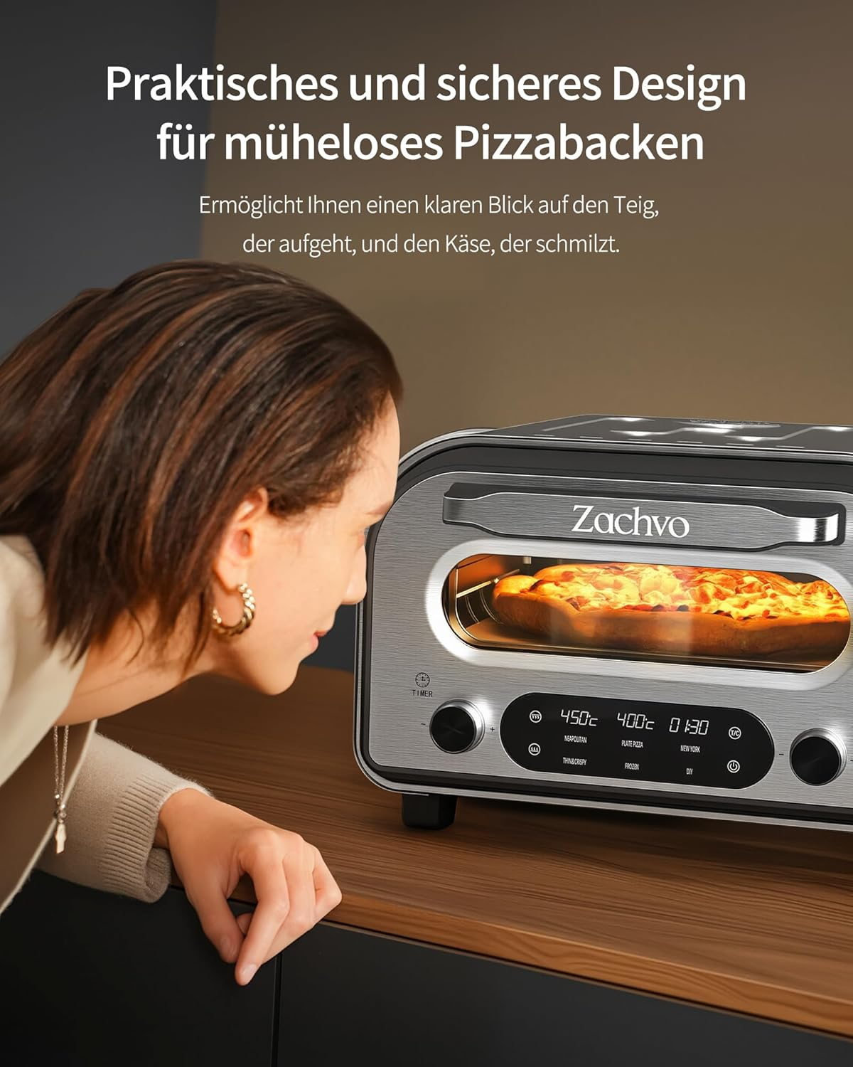 Eine Frau schaut erwartungsvoll in einen modernen silbernen Ofen, in dem eine Pizza backt.