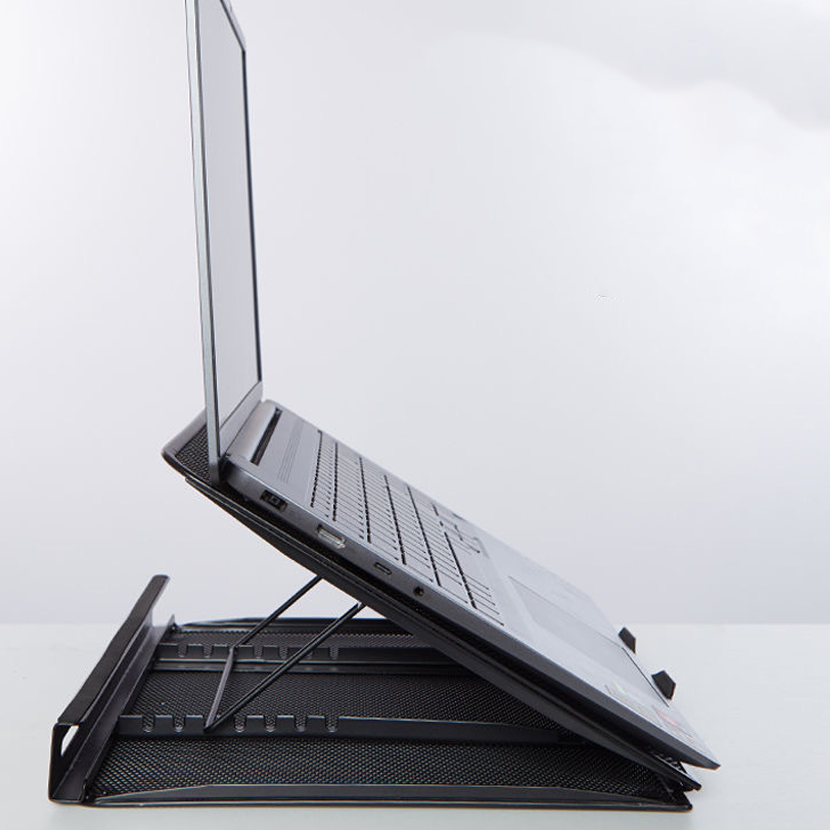 Ein Laptop steht seitlich auf einem verstellbaren, schwarzen Metallständer auf einer weißen Oberfläche.