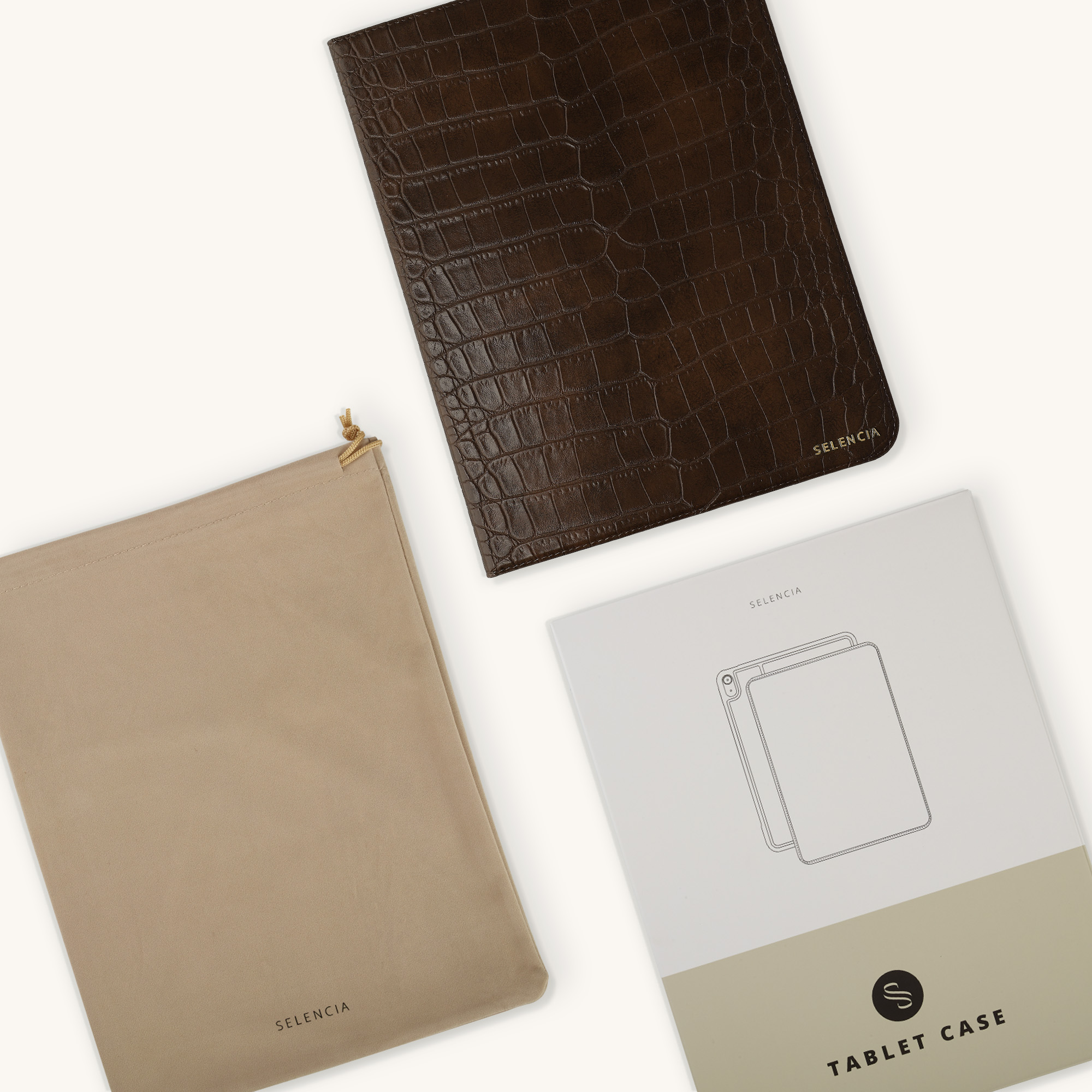 Bruine croco-lederen tablethoes, beige stoffen tasje en witte verpakking op lichte achtergrond.