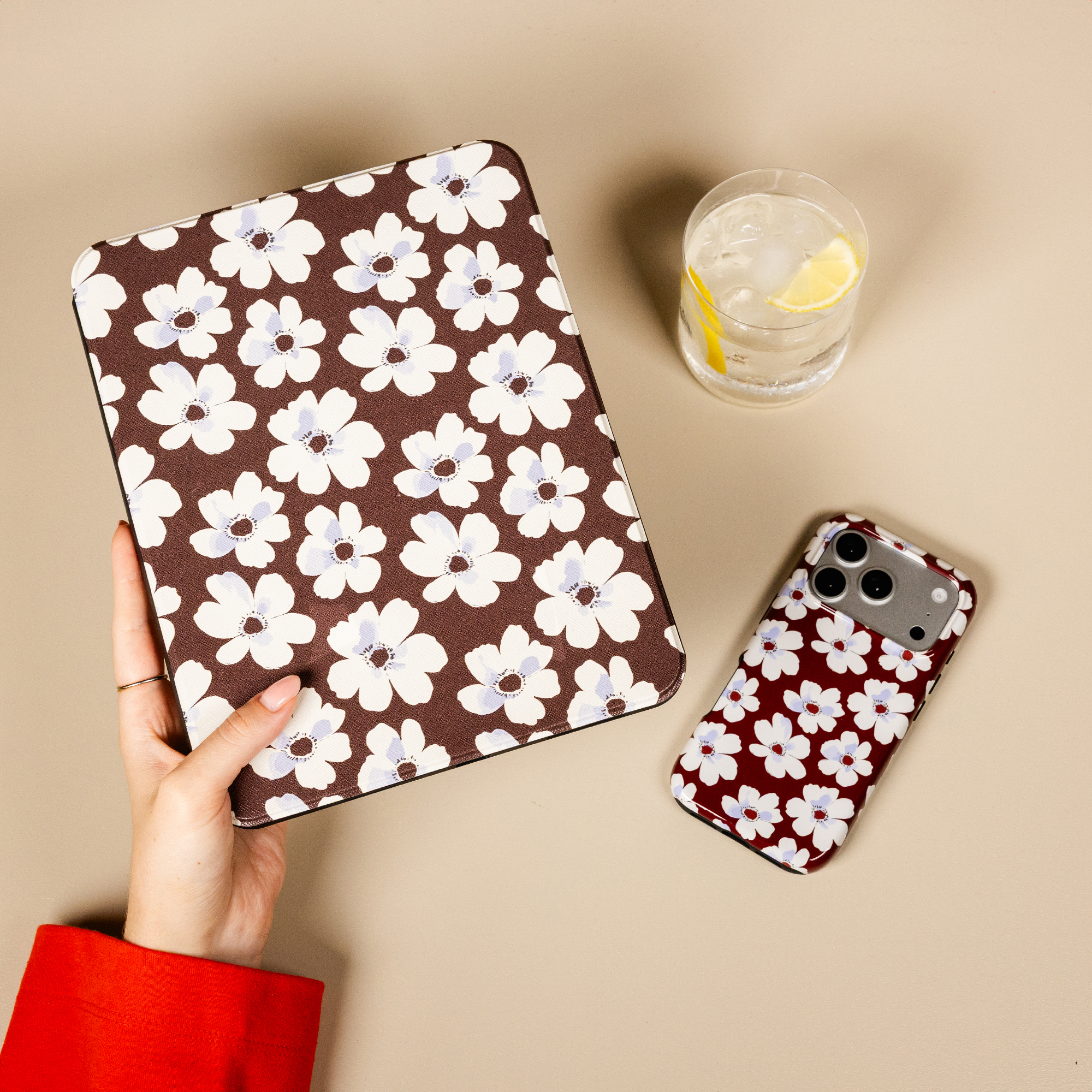 Une main tient une tablette marron à motif floral blanc près d'un téléphone et d'une boisson assortis.
