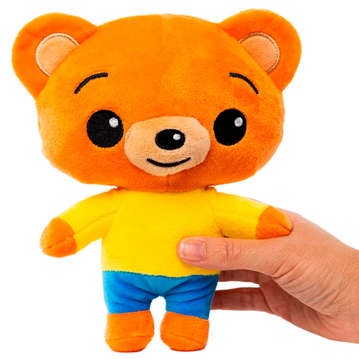 Un oso de peluche naranja con parte superior amarilla y pantalones azules es sostenido por una mano.