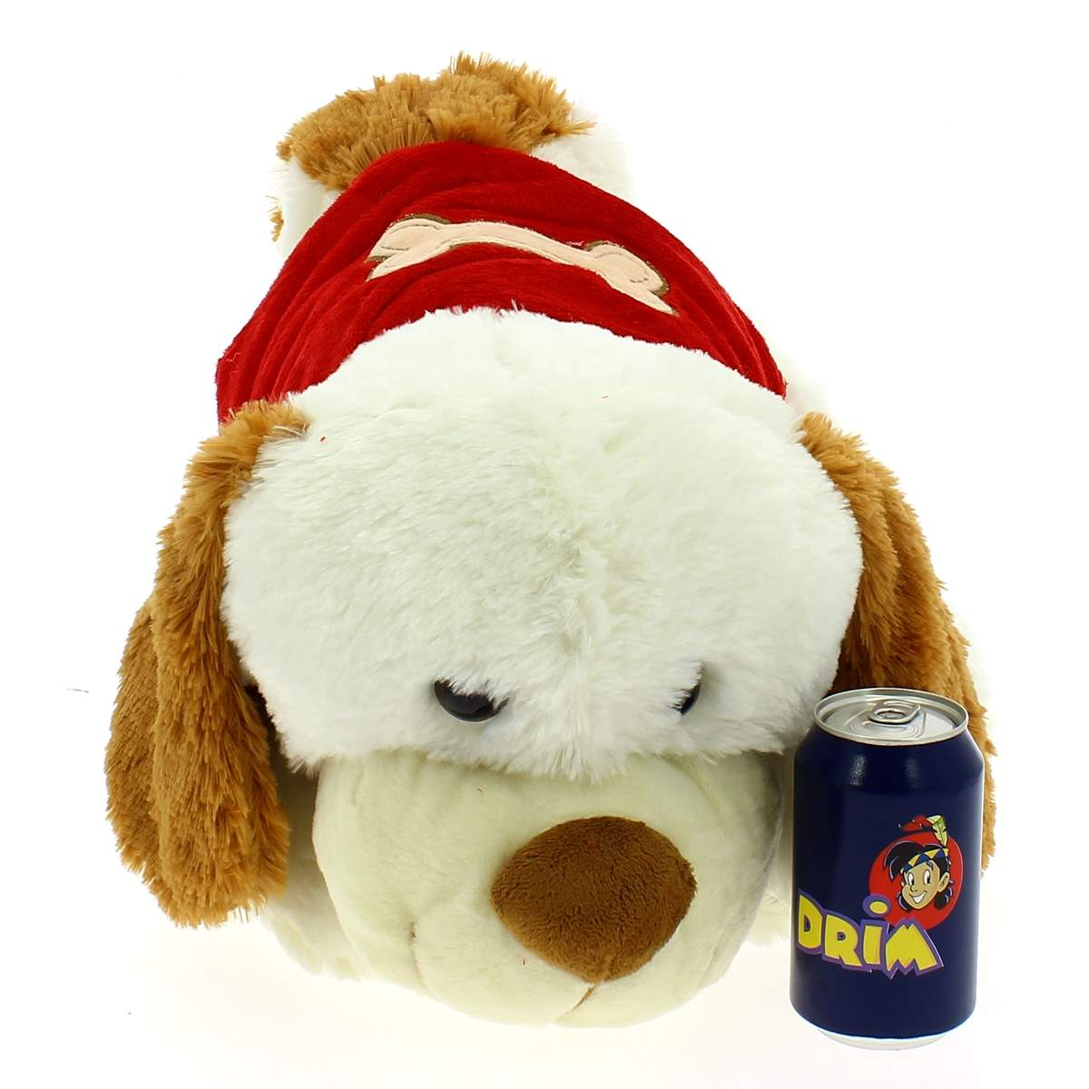 Un perro de peluche blanco con ropa roja yace junto a una lata de refresco azul.