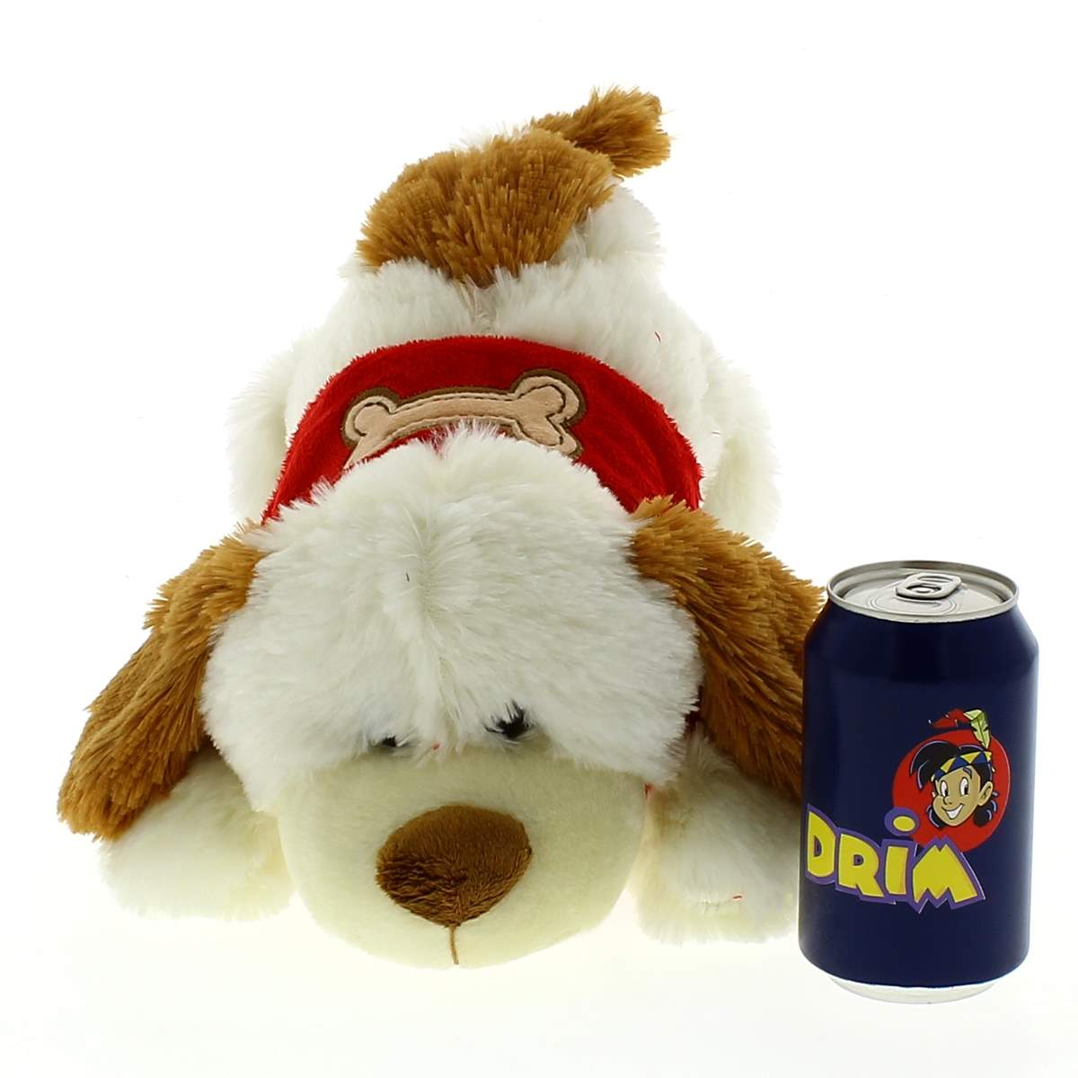 Un peluche de perro blanco y marrón al lado de una lata de refresco azul sobre fondo blanco.