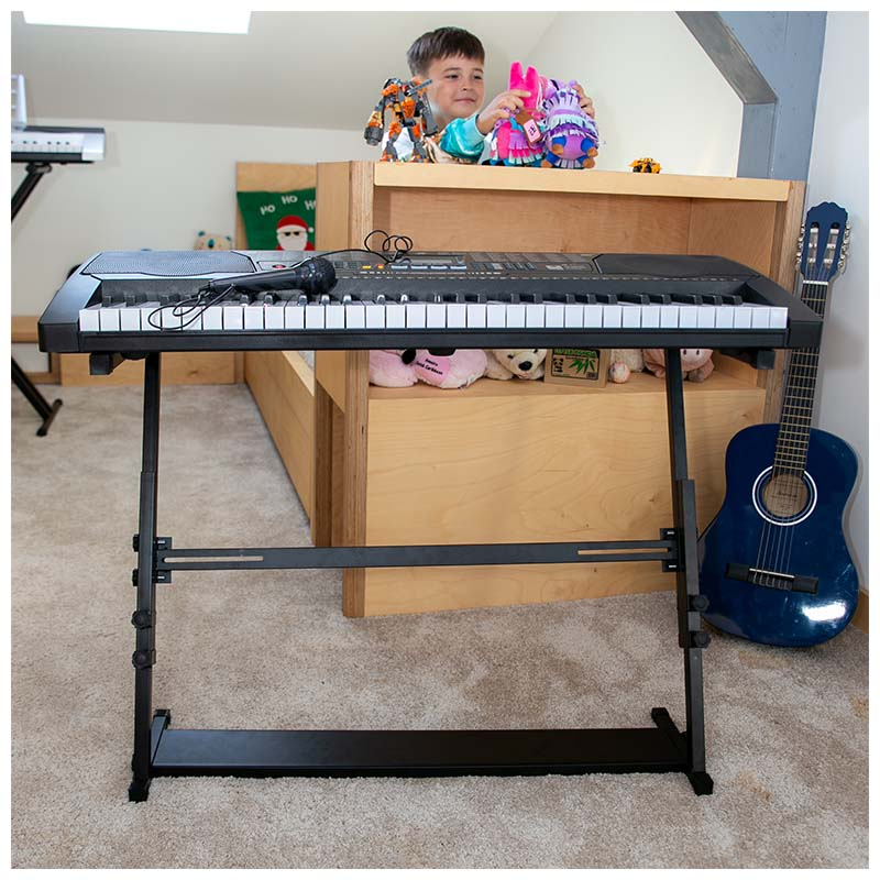 Ein schwarzes Keyboard auf einem Ständer mit Mikrofon, eine blaue Gitarre und ein Junge im Hintergrund.