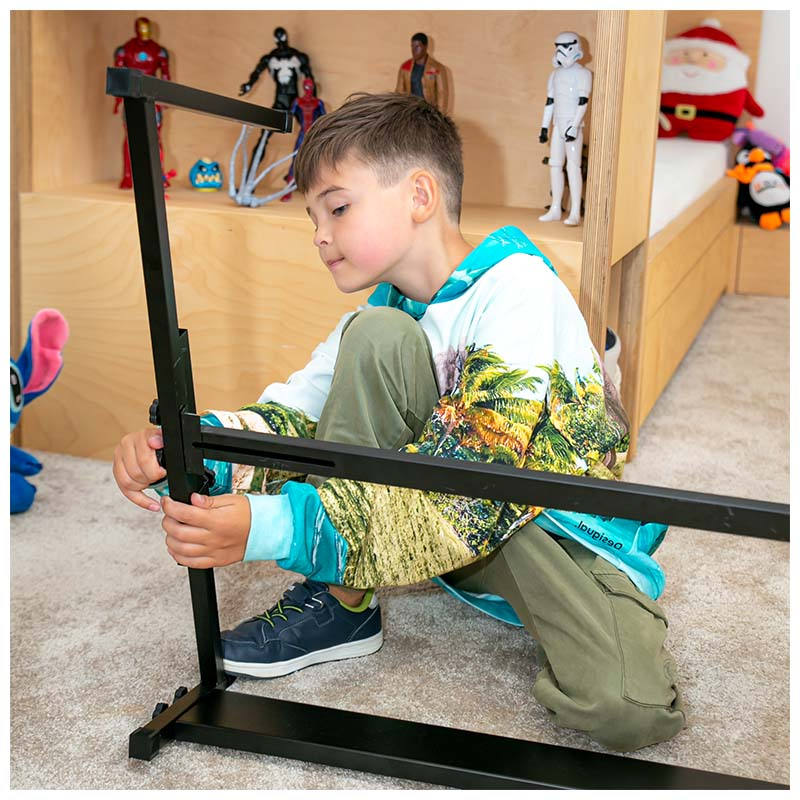 Ein Junge montiert einen schwarzen Metallständer im Zimmer mit Spielzeugregal im Hintergrund.