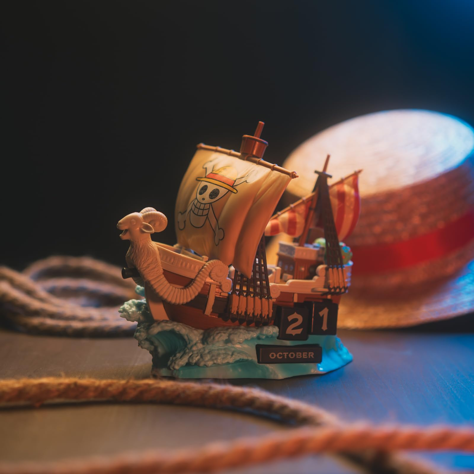 Un barco pirata miniatura con vela de calavera descansa junto a un sombrero de paja y cuerda.