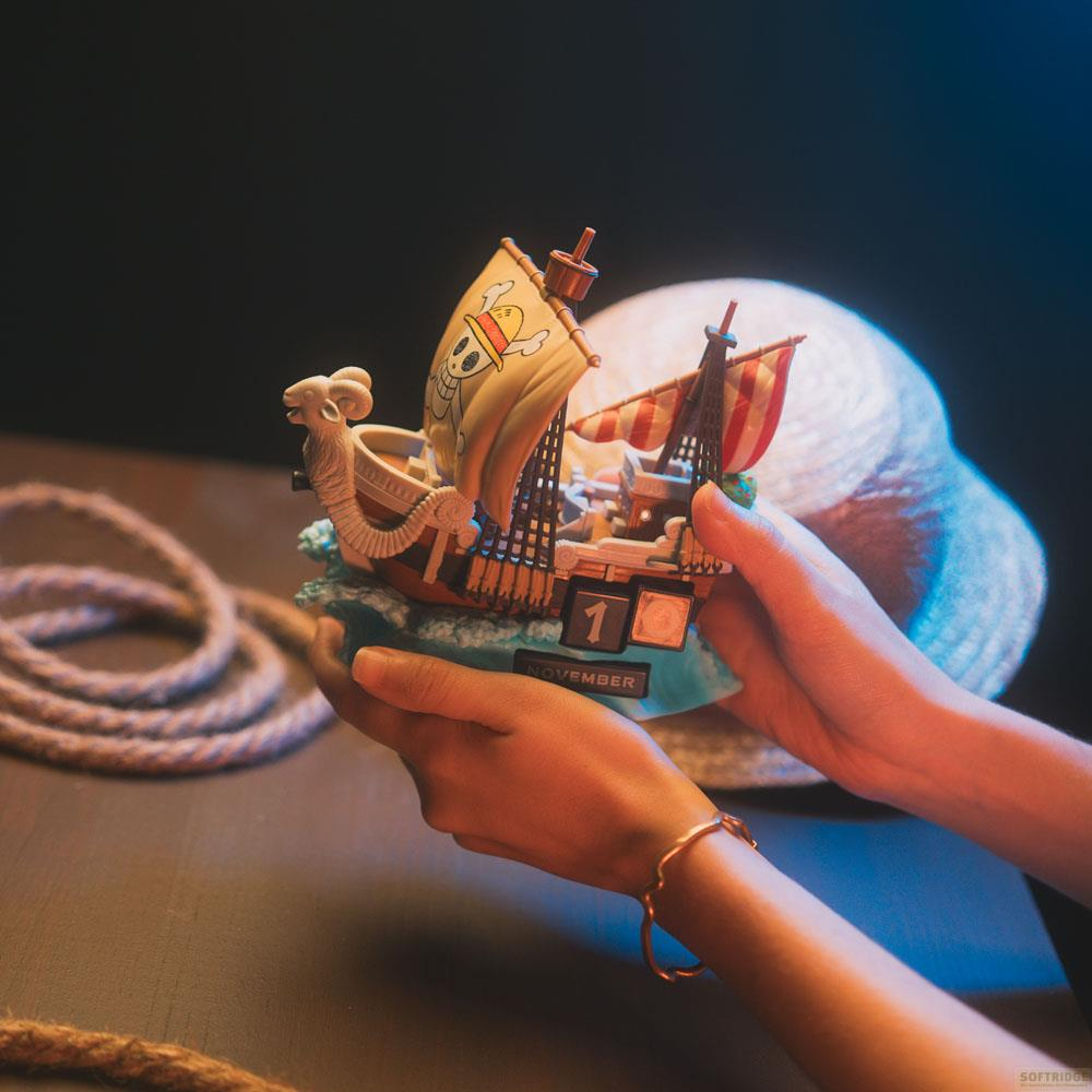 Una persona sostiene una figura de barco de One Piece, con un sombrero de paja y una cuerda al fondo.