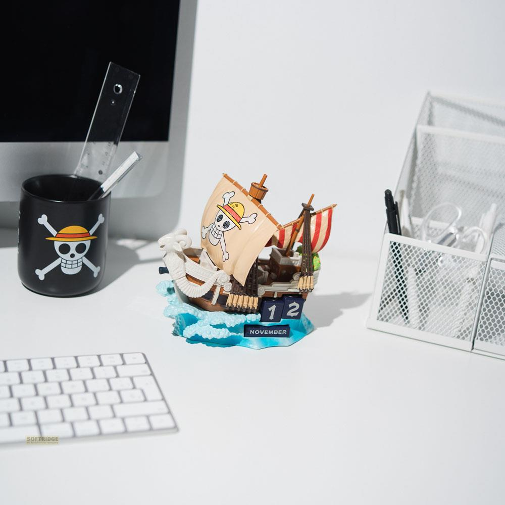 Un calendario con modelo de barco de One Piece en un escritorio blanco junto a portalápices y un teclado.