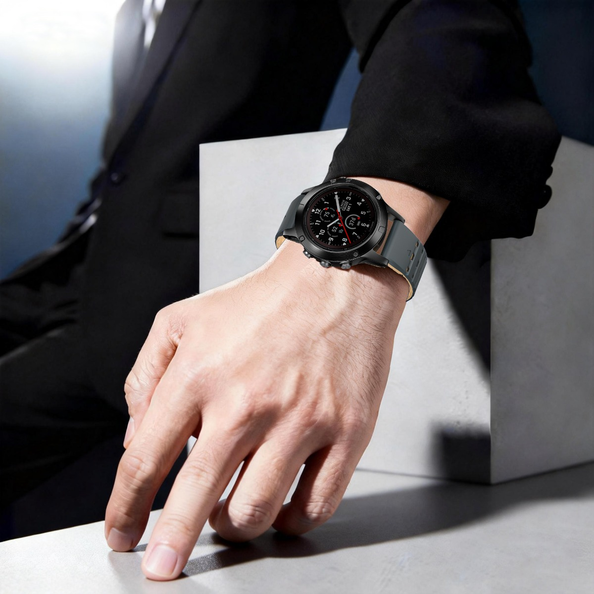 Ein Mann im schwarzen Anzug trägt eine stilvolle schwarze Armbanduhr mit grauem Lederarmband an der Hand.